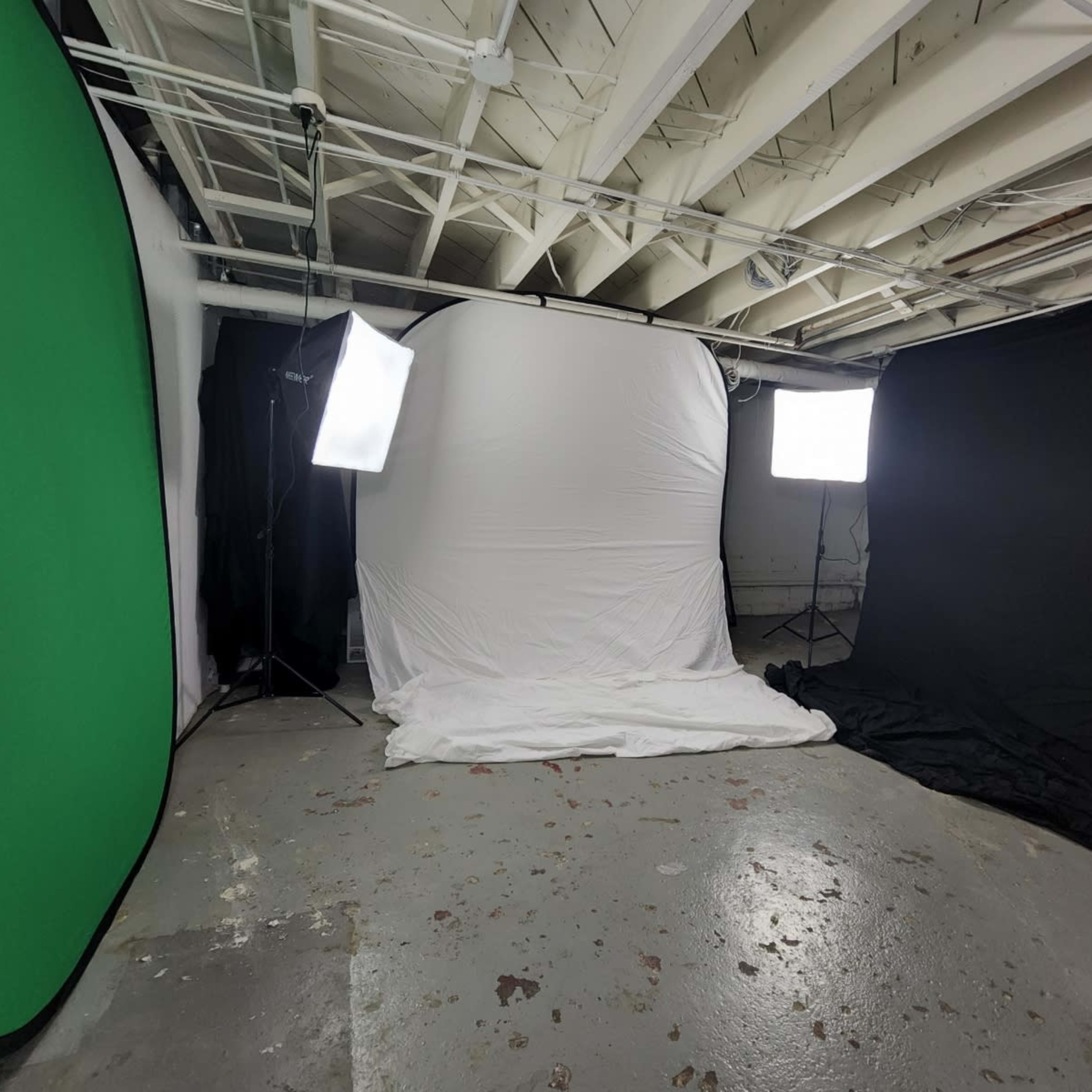 A photography setup in a basement, featuring a white backdrop surrounded by a green backdrop, a black backdrop, and two softbox lights.