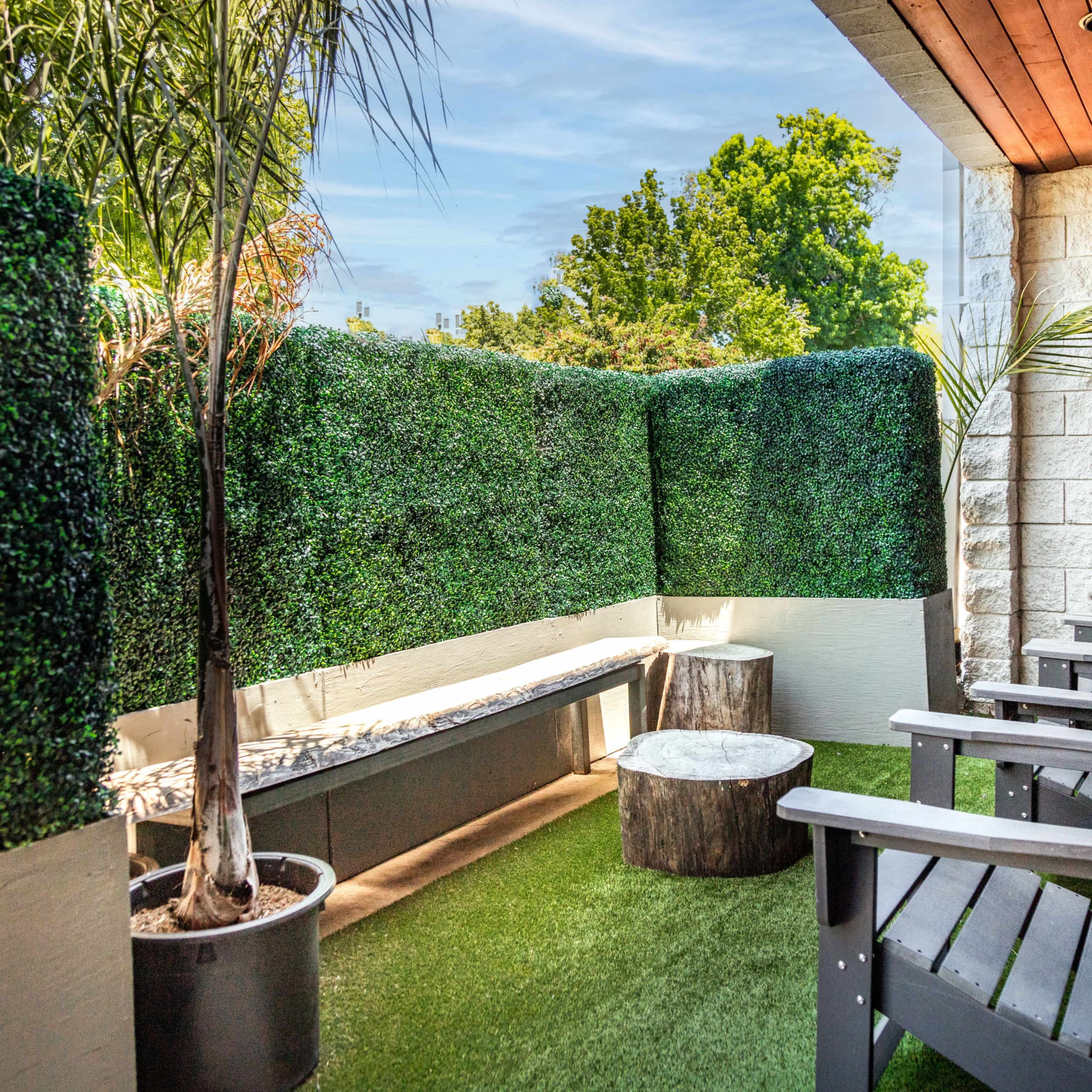 A small outdoor terrace with wooden chairs, a bench, and greenery-lined walls.