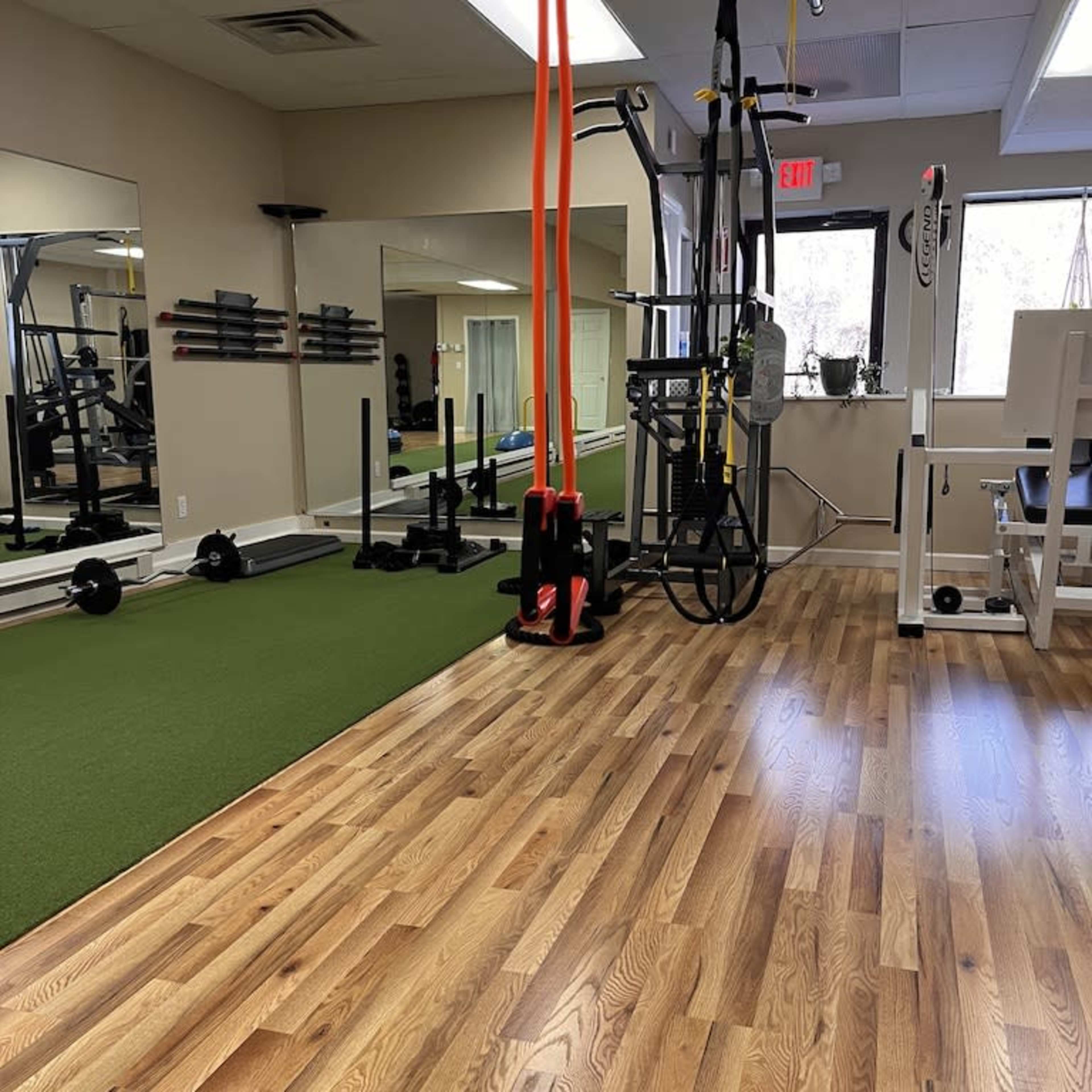 A fitness studio with exercise equipment, including weights and suspension straps, and a section of green turf flooring.