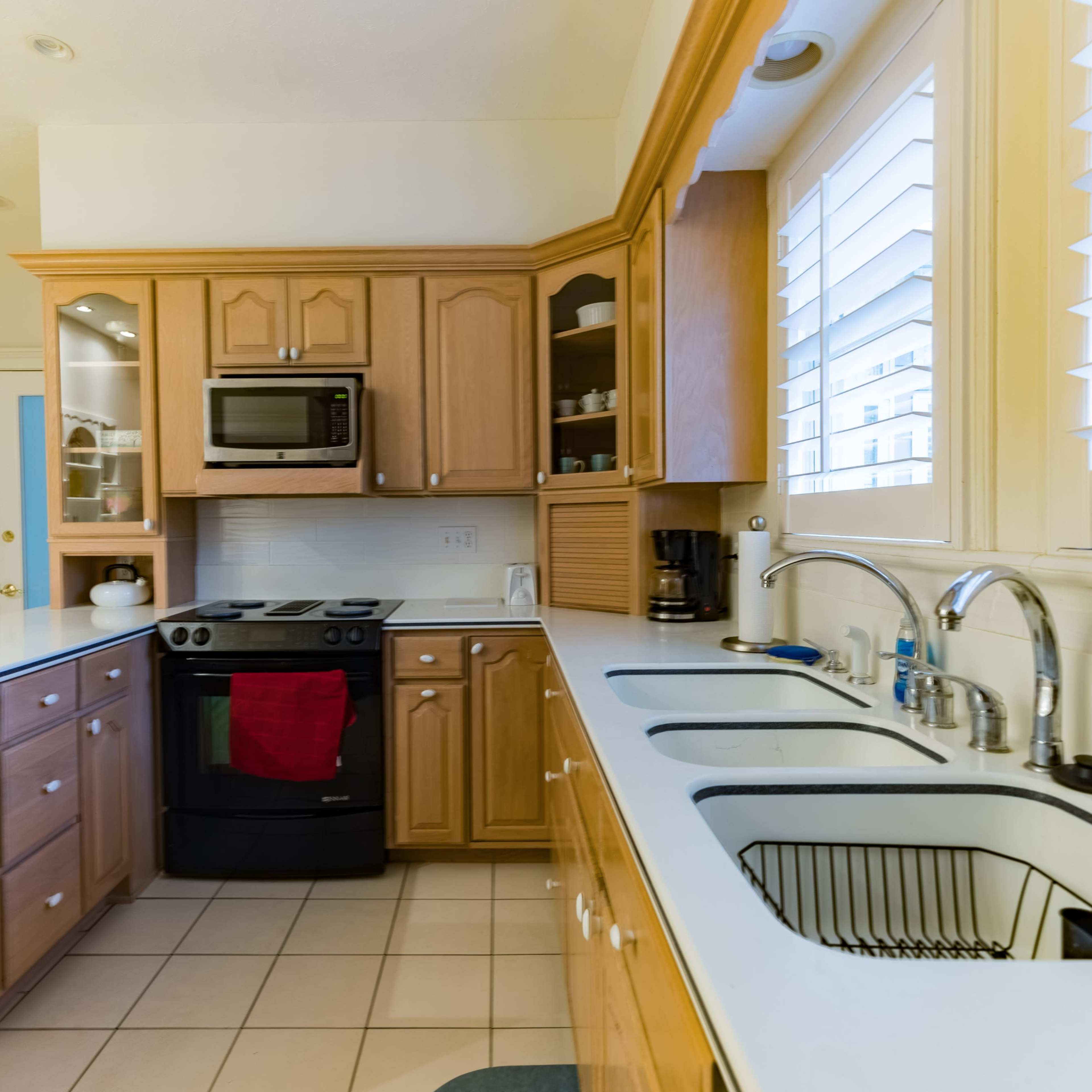 A kitchen featuring wooden cabinetry, a black stove, a microwave, and a double sink positioned along a tiled floor.