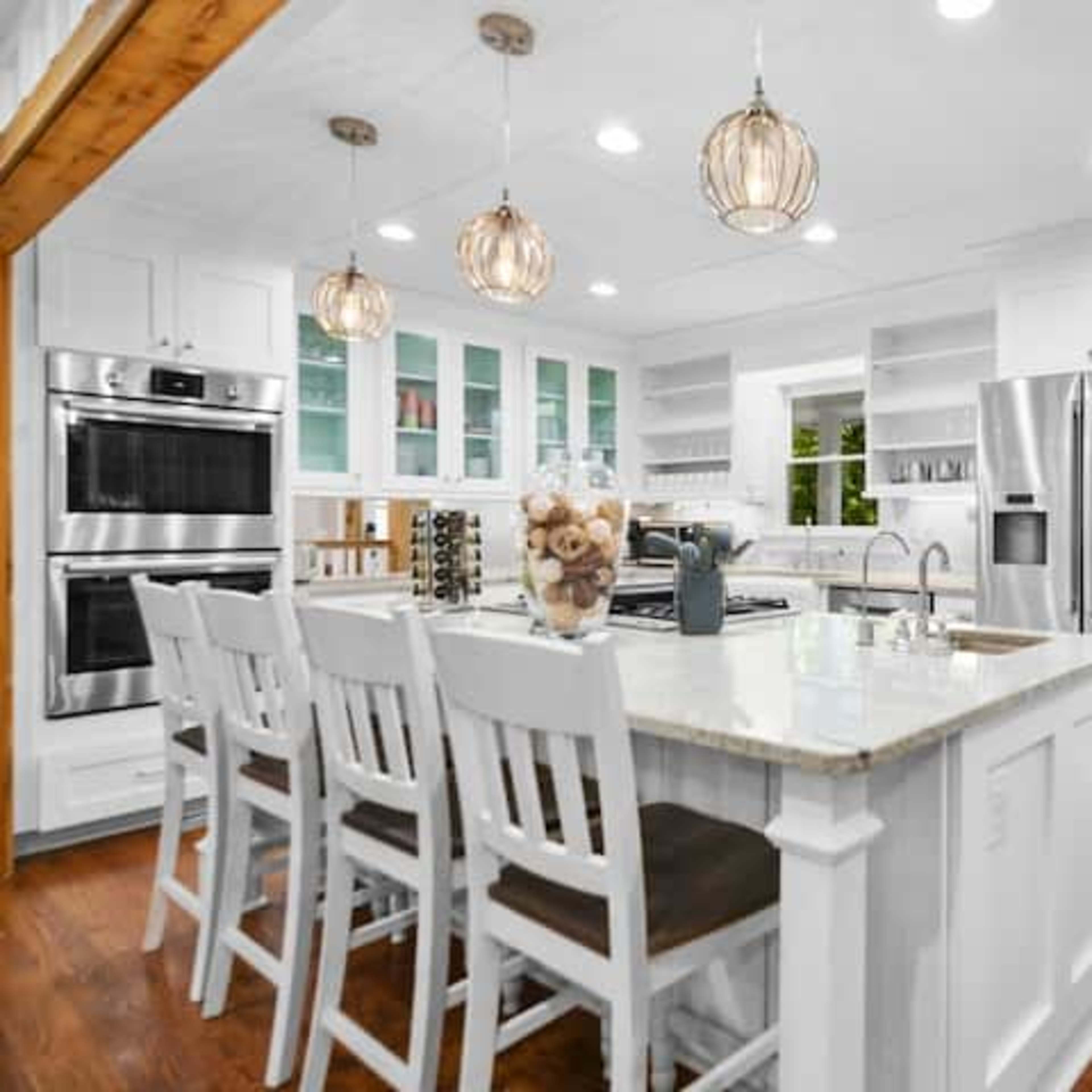 A bright kitchen features white cabinetry, stainless steel appliances, and an island with seating for six.