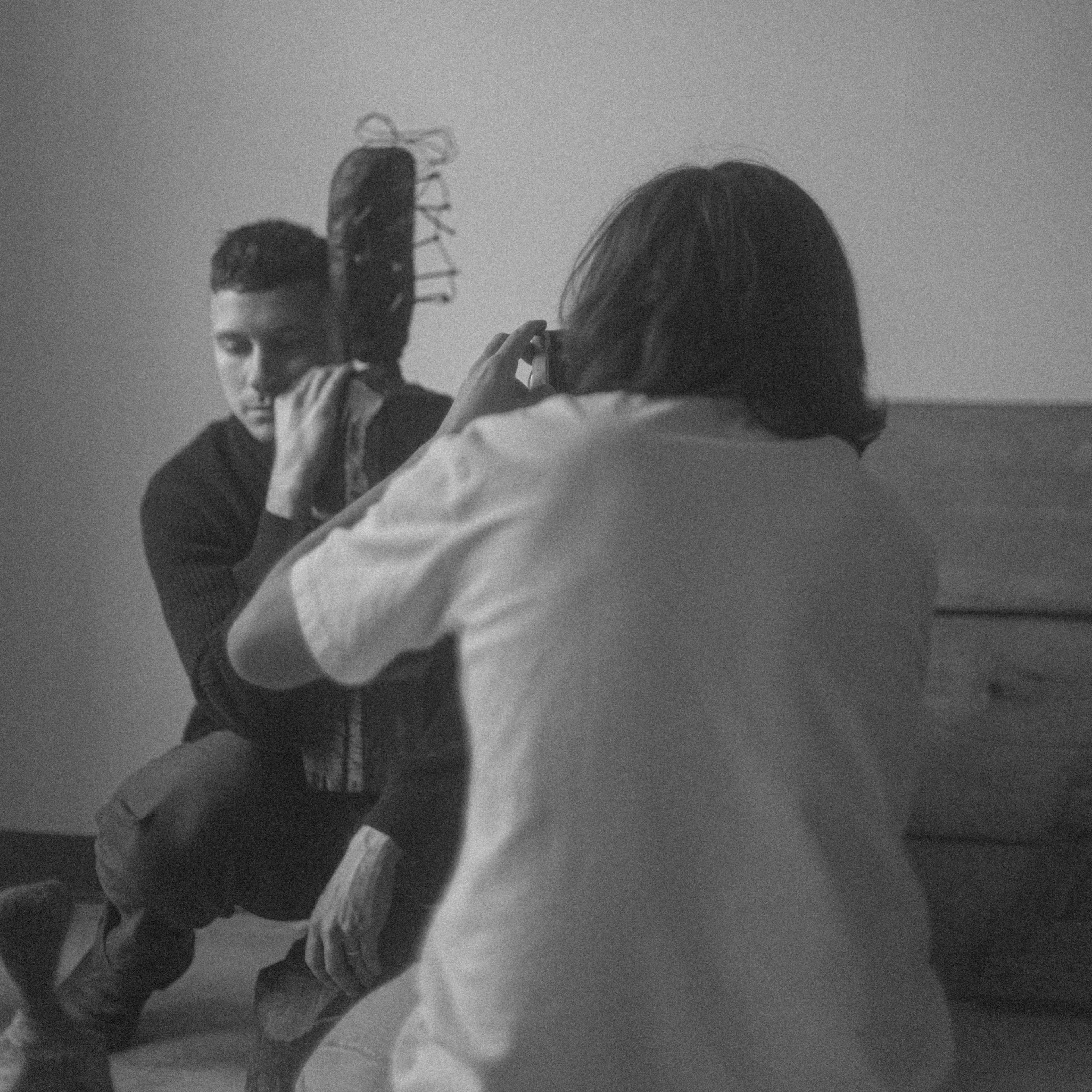 A person poses with a guitar while another individual takes their photograph.