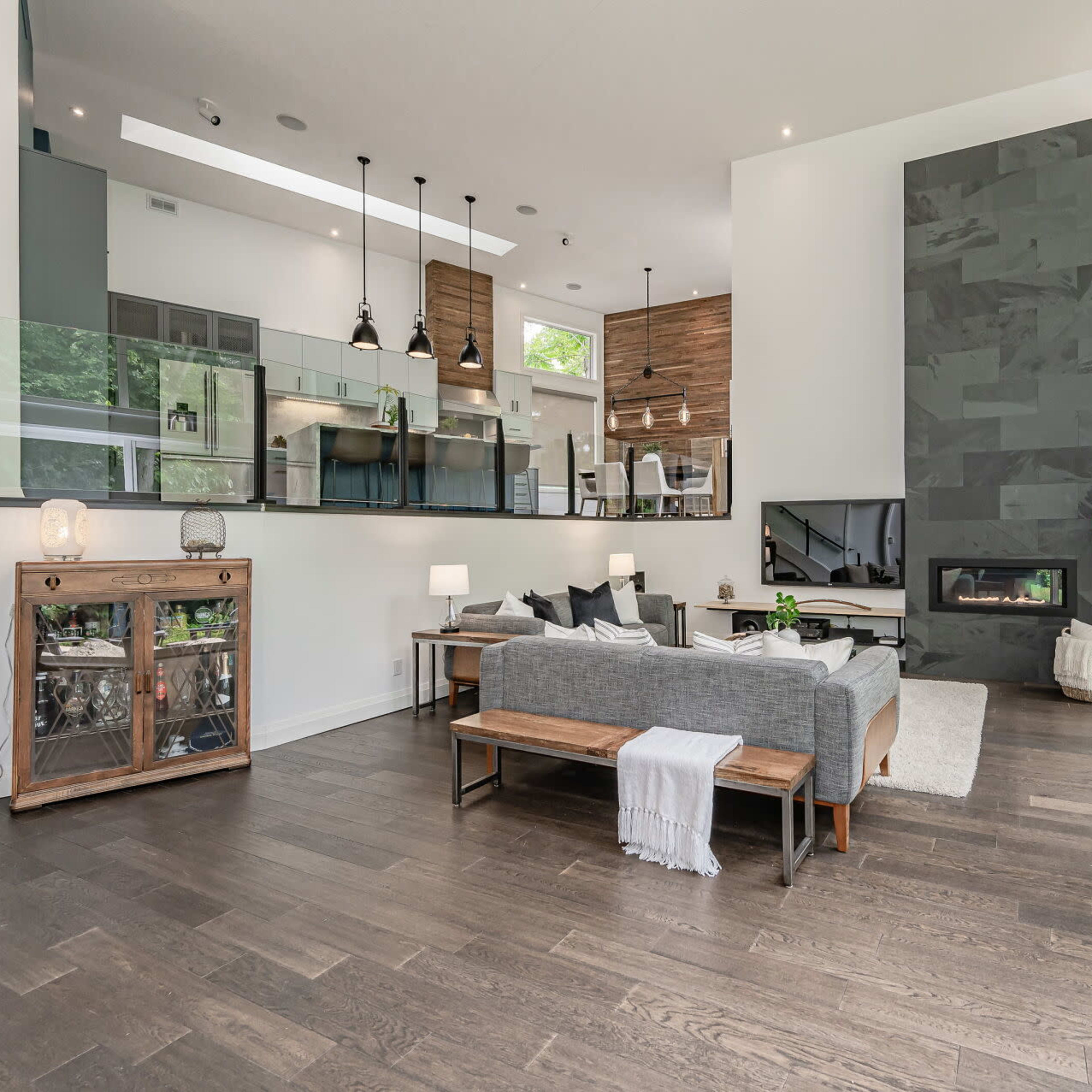 A modern living room with large windows, a sleek fireplace, and a glass partition separating it from a contemporary kitchen.