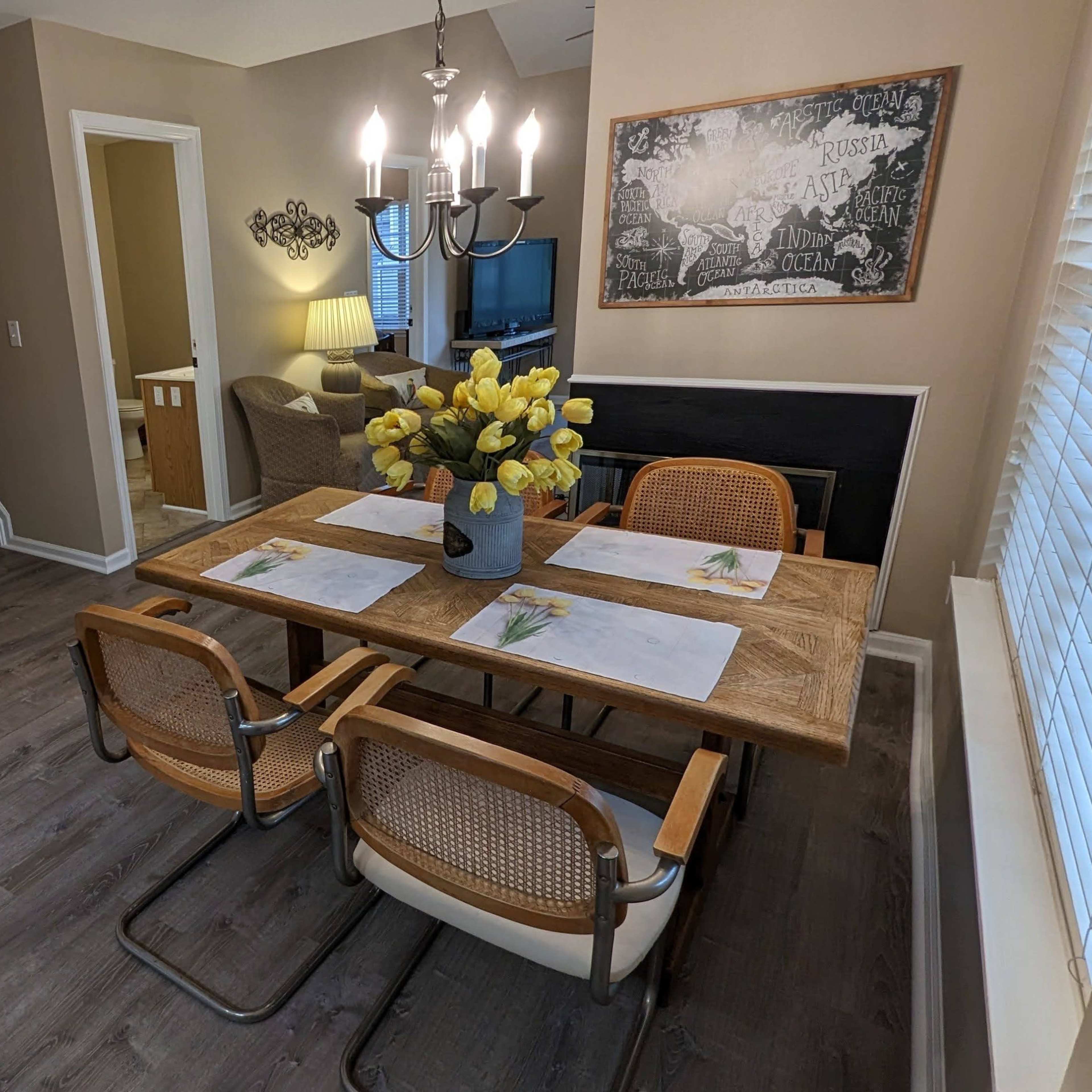 A dining area featuring a wooden table with chairs, a vase of yellow flowers, and a staircase leading to another level.