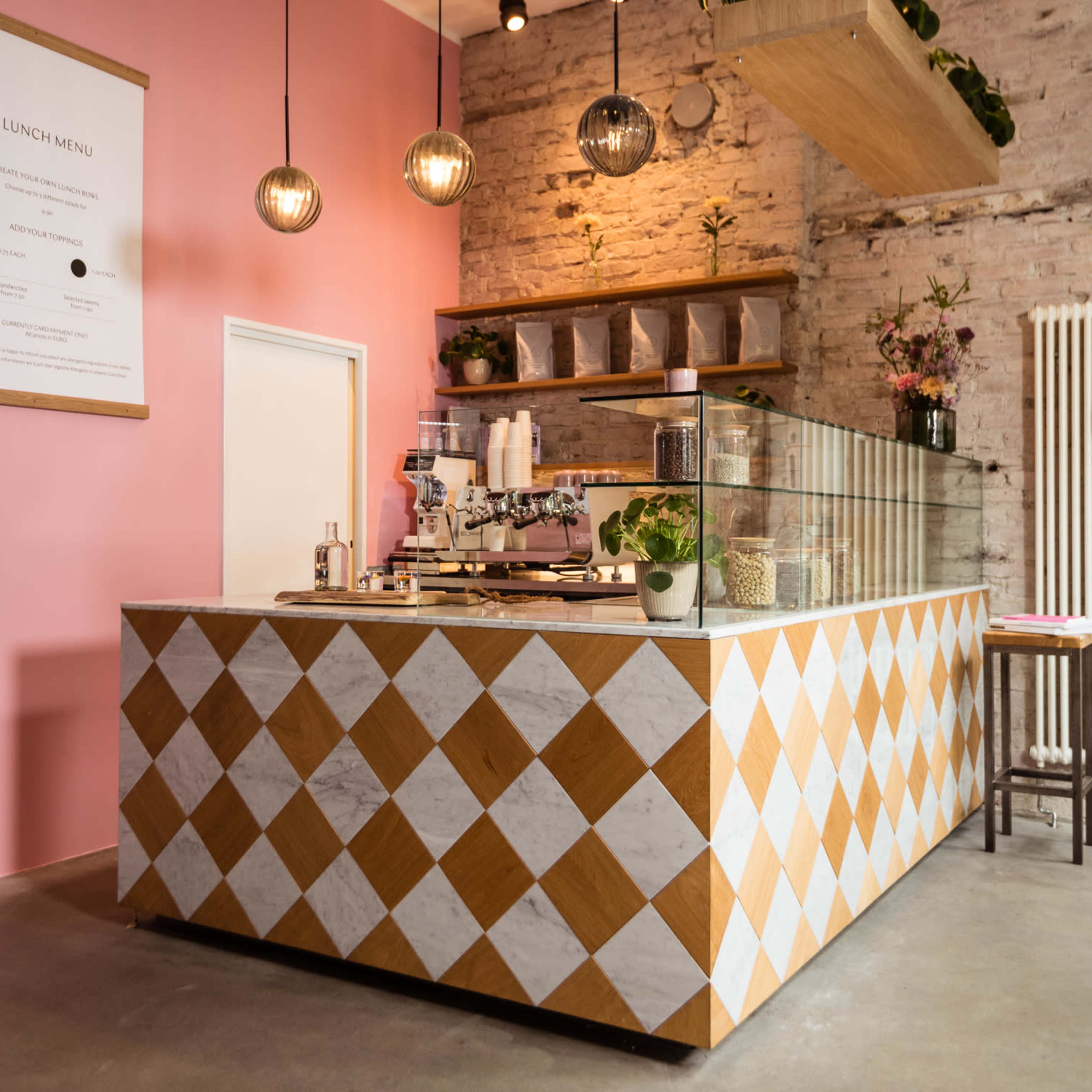 A cafe interior with a colorful diamond-patterned counter, light pink walls, and decorative lighting fixtures.