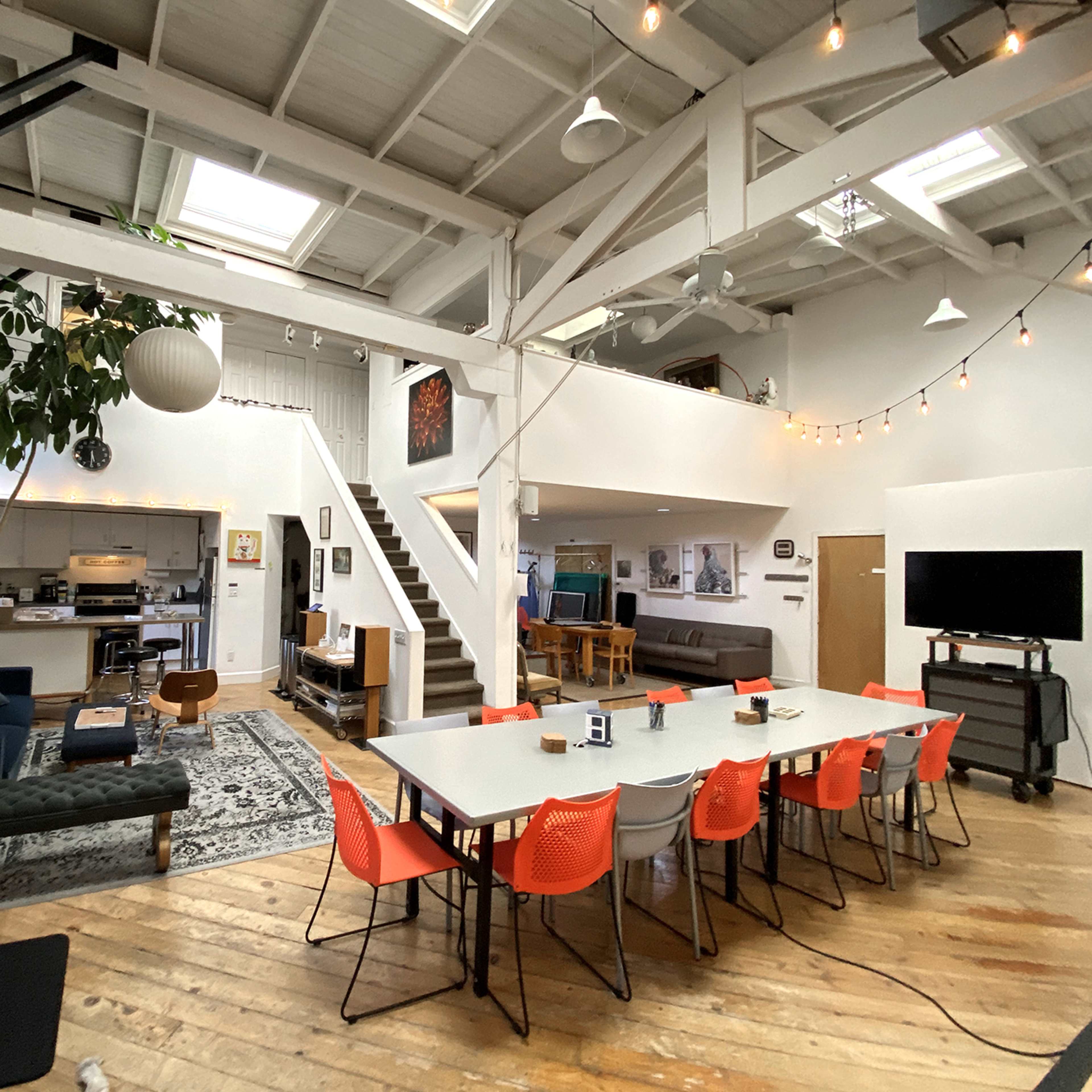 A large room with a long table and colorful chairs on one side, and an outdoor patio area with wooden seating and a fire pit on the other.