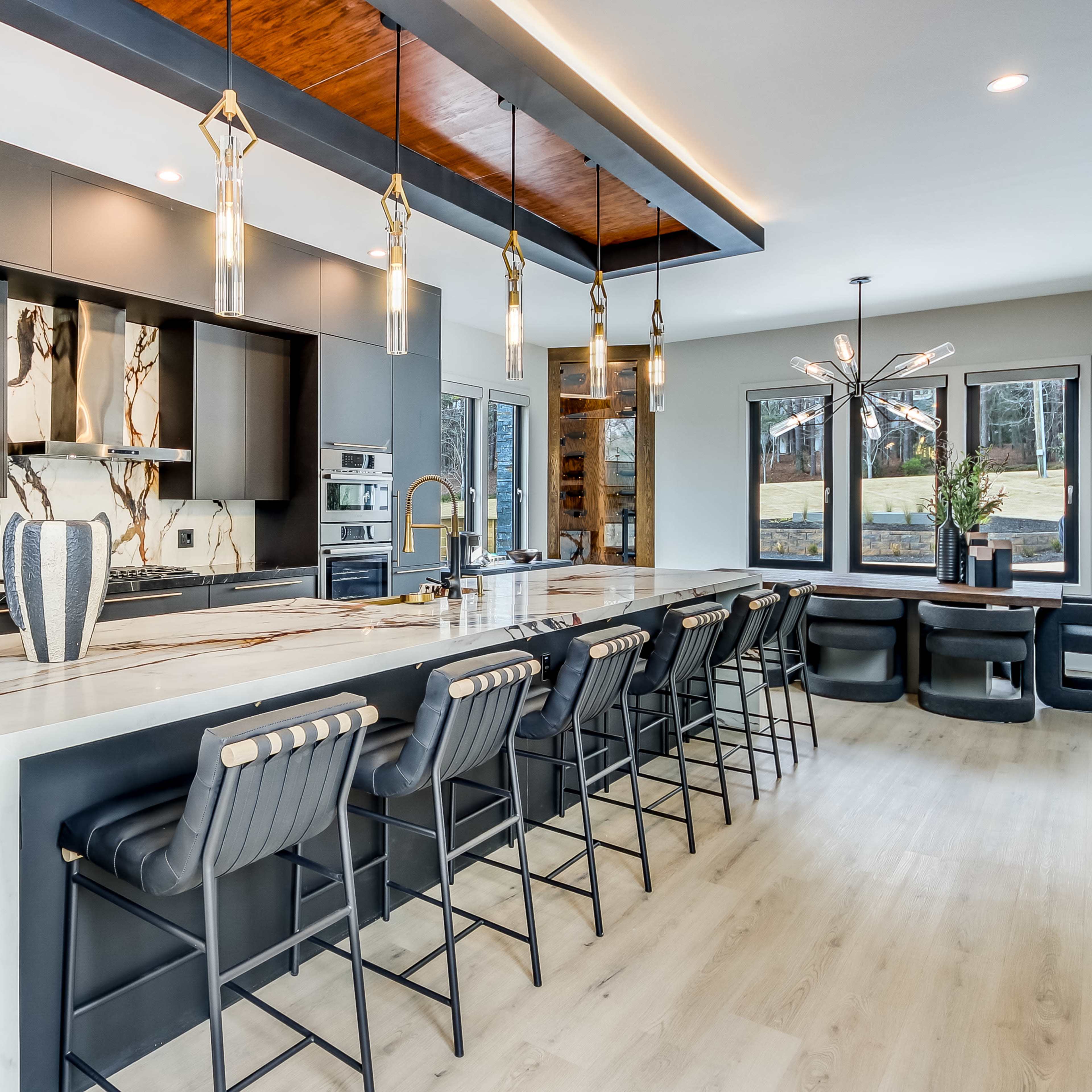 A modern kitchen featuring a long marble island with black bar stools, sleek cabinetry, and pendant lighting.