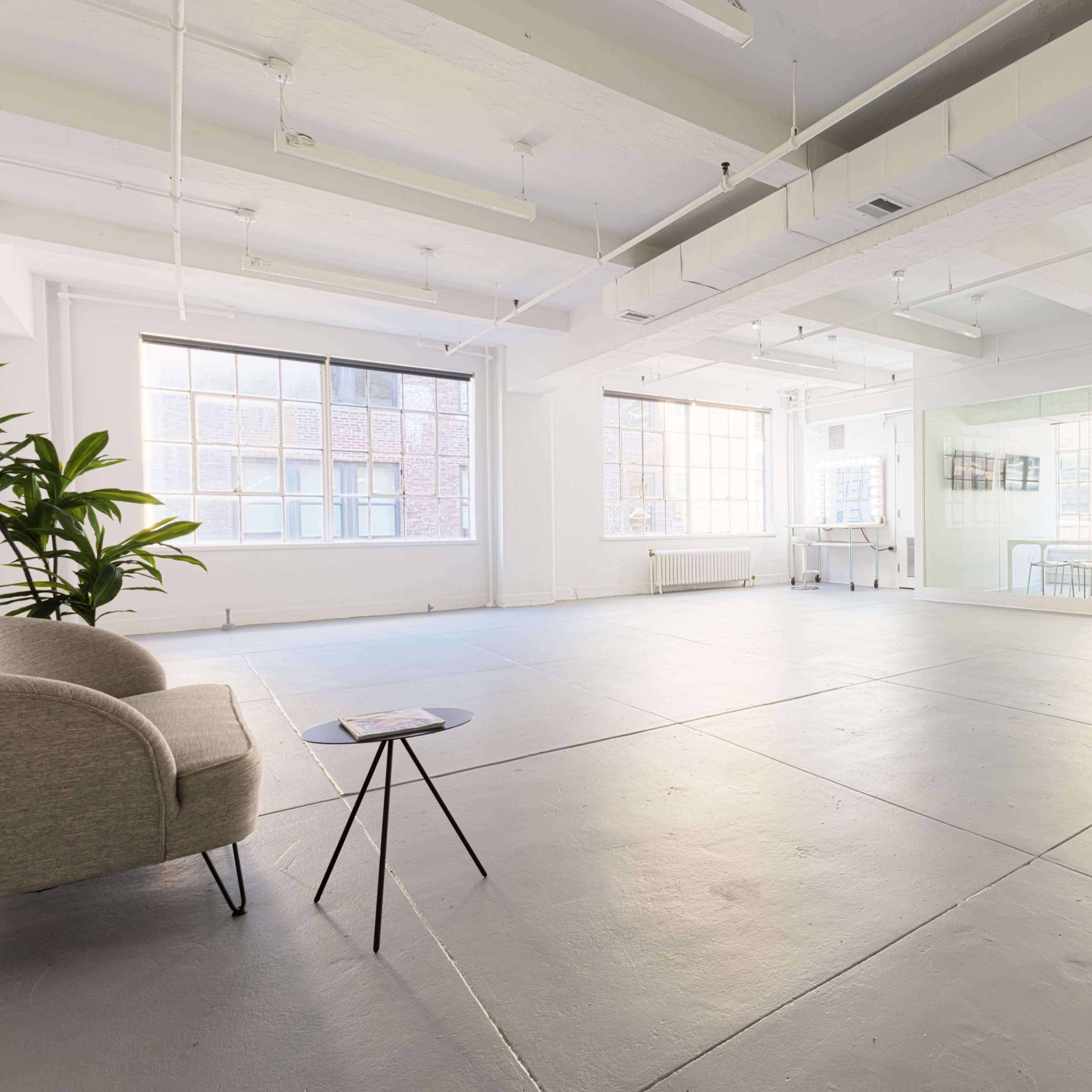 A spacious, well-lit room with large windows, a small table, and a couch in one corner.