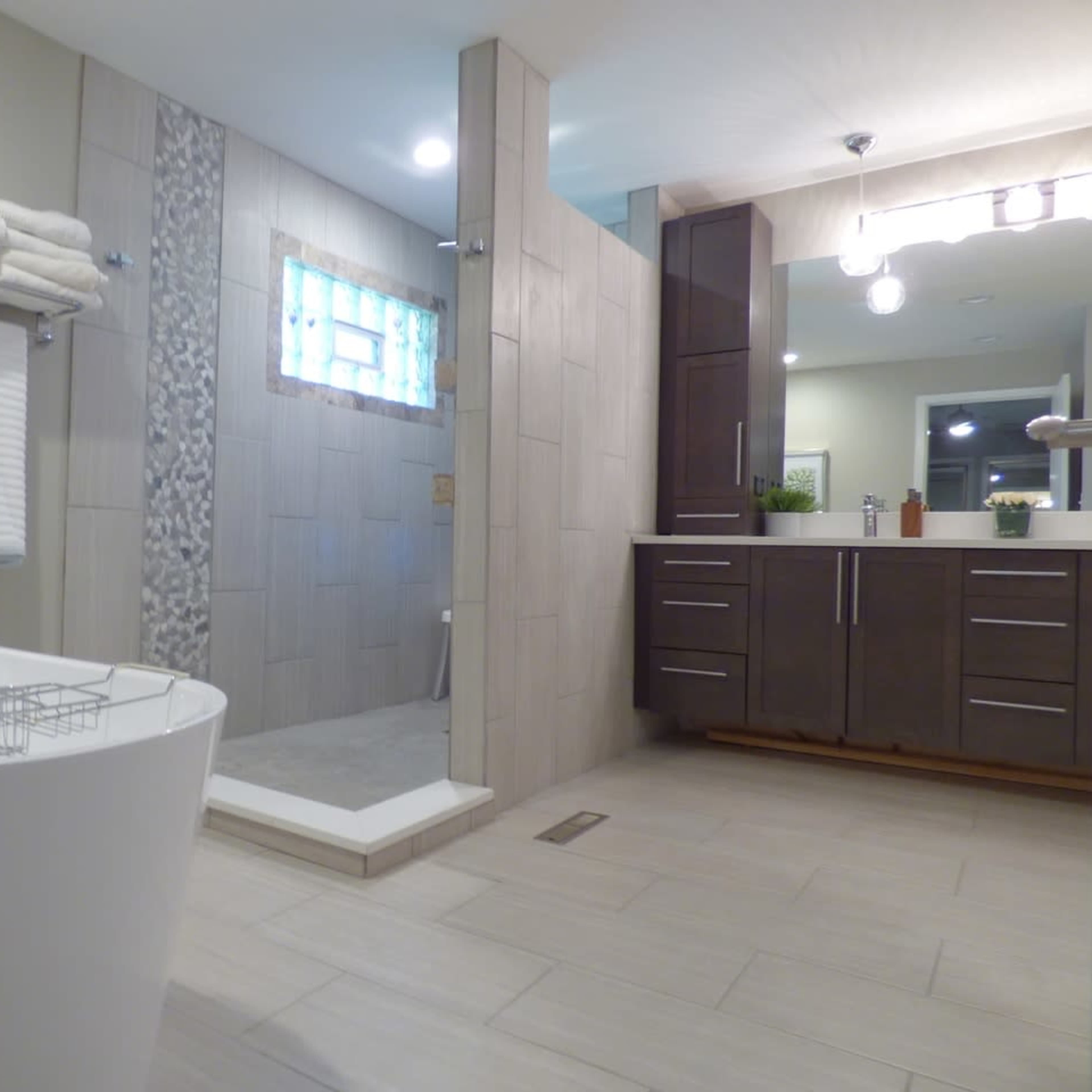 A modern bathroom featuring a freestanding bathtub, a walk-in shower with a stone accent wall, and a wooden vanity with multiple drawers.