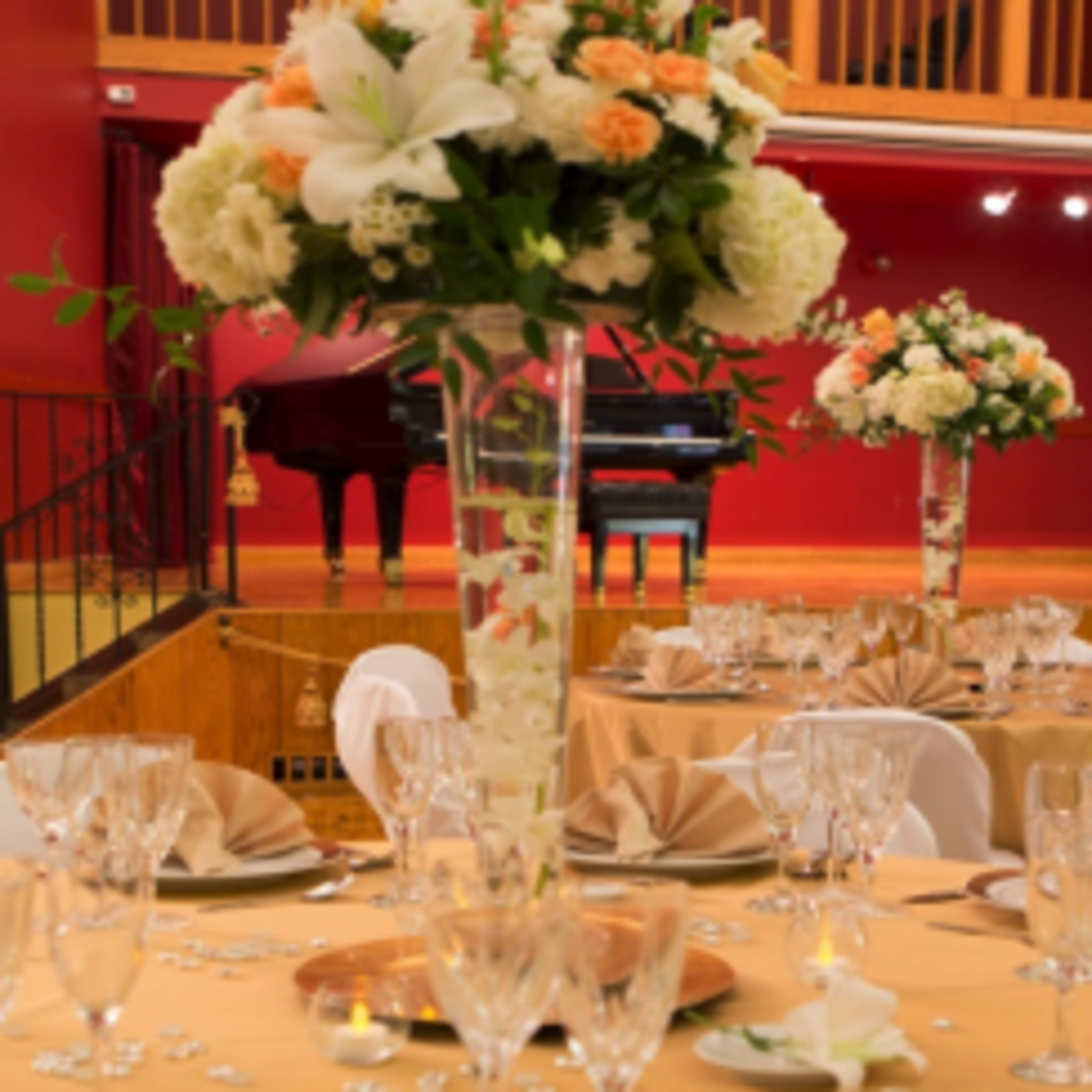 A banquet hall set for an event, featuring elegantly arranged tables with floral centerpieces and a piano in the background.