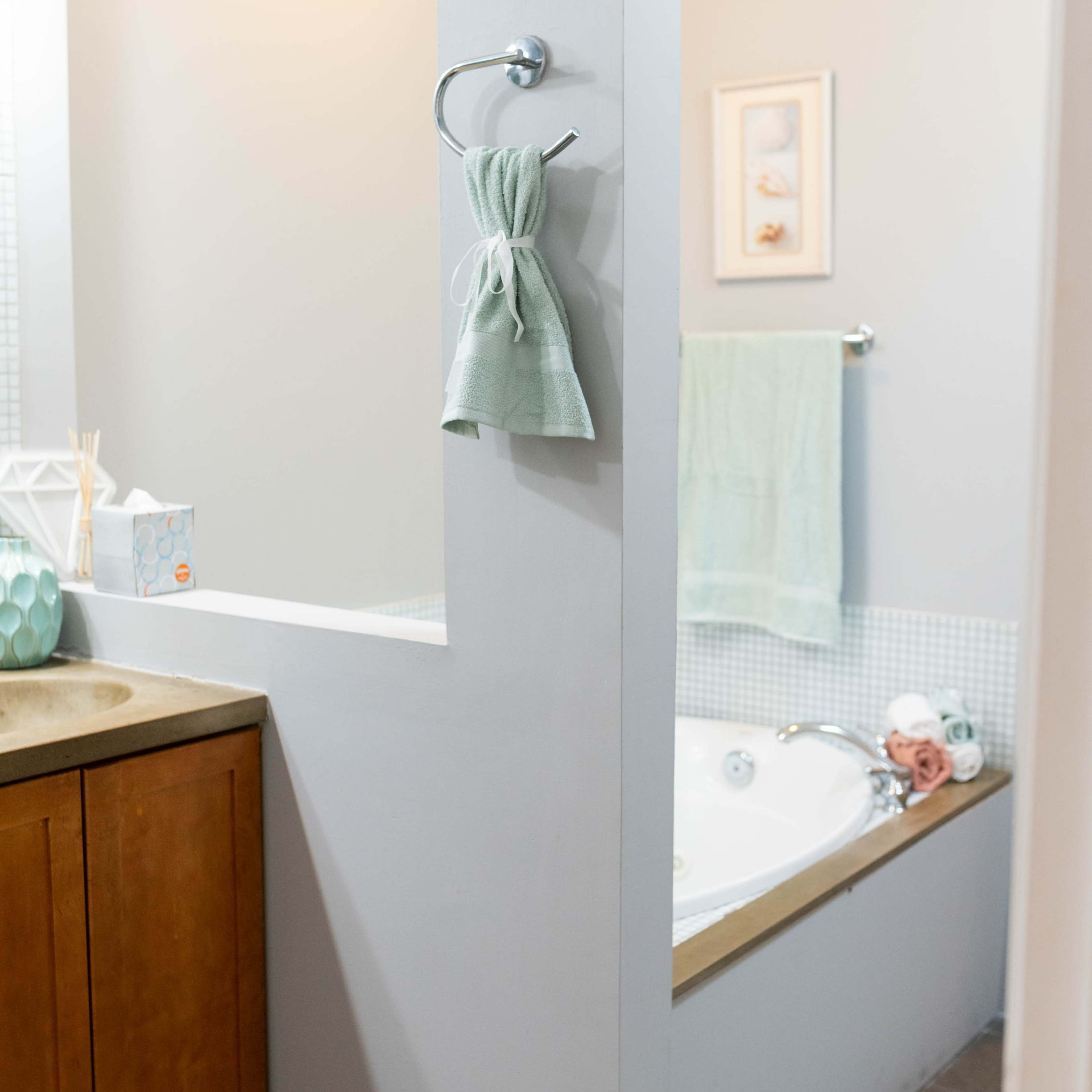 A bathroom with a wooden vanity and a tub partially enclosed by a low wall, along with a towel hanging on a rack.