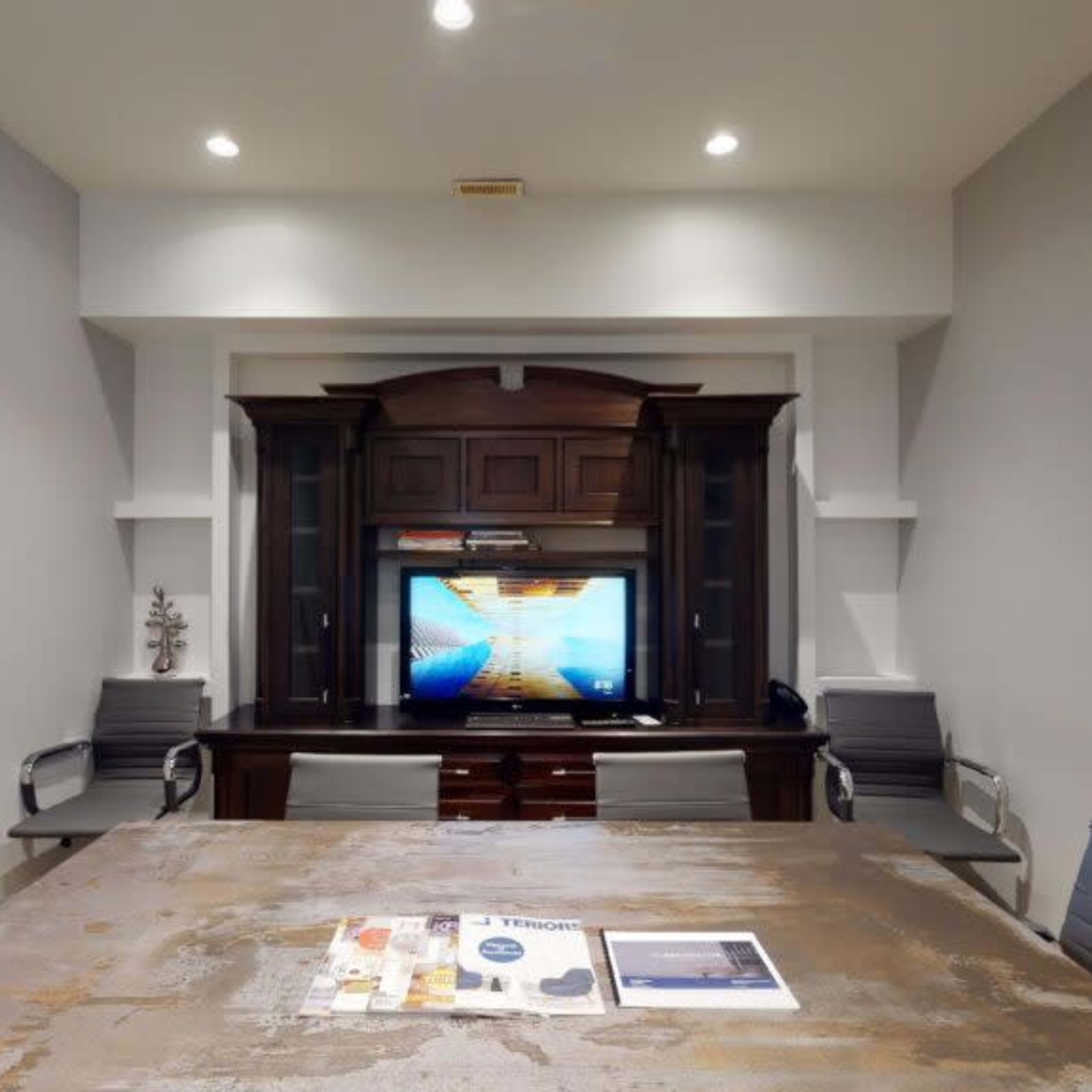 A modern conference room with a large wooden table, metal chairs, and a wall-mounted television displaying a graphic on a media console.