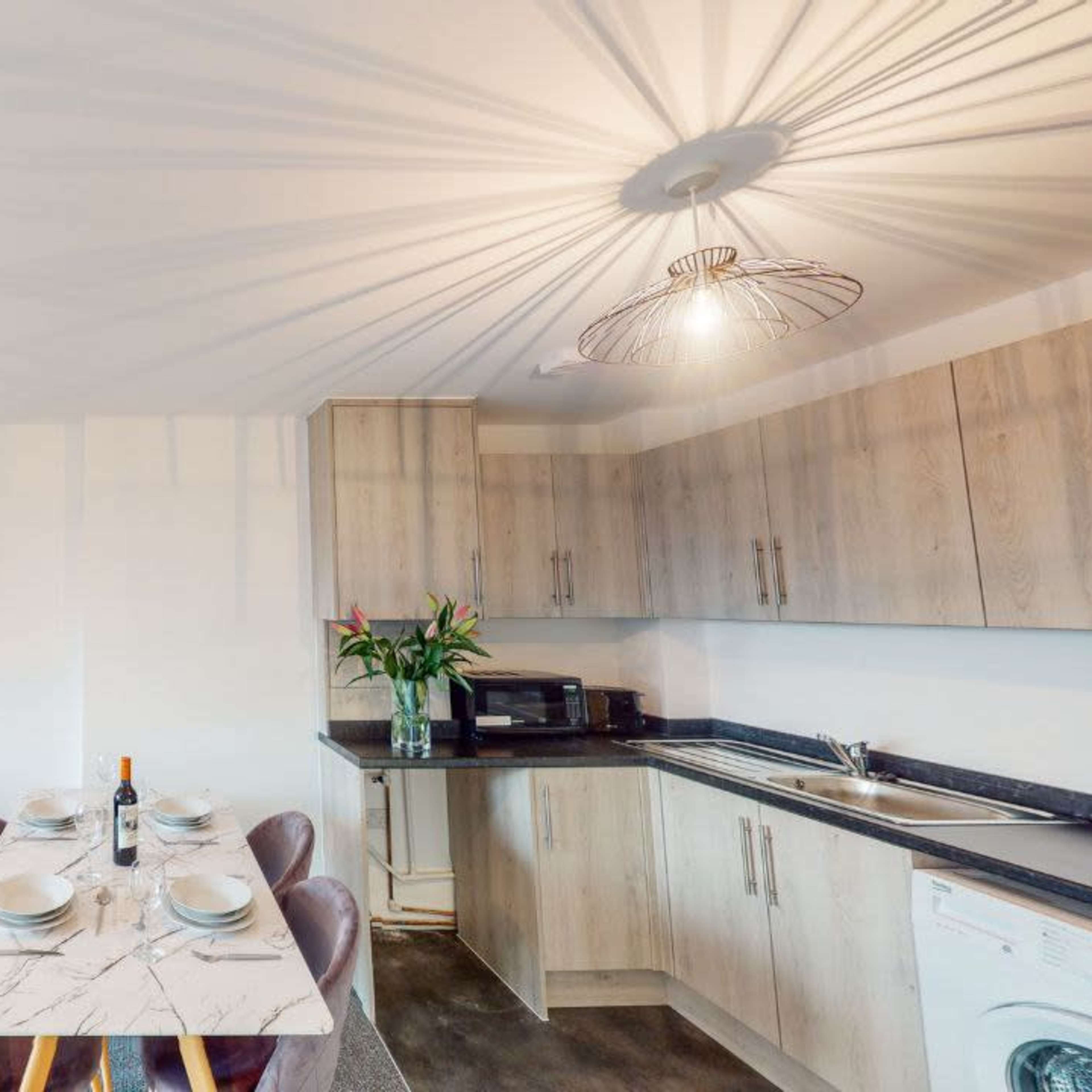 A modern kitchen and dining area feature a marble table set for four, a gray sofa with colorful cushions, and pendant lighting casting shadows on the ceiling.