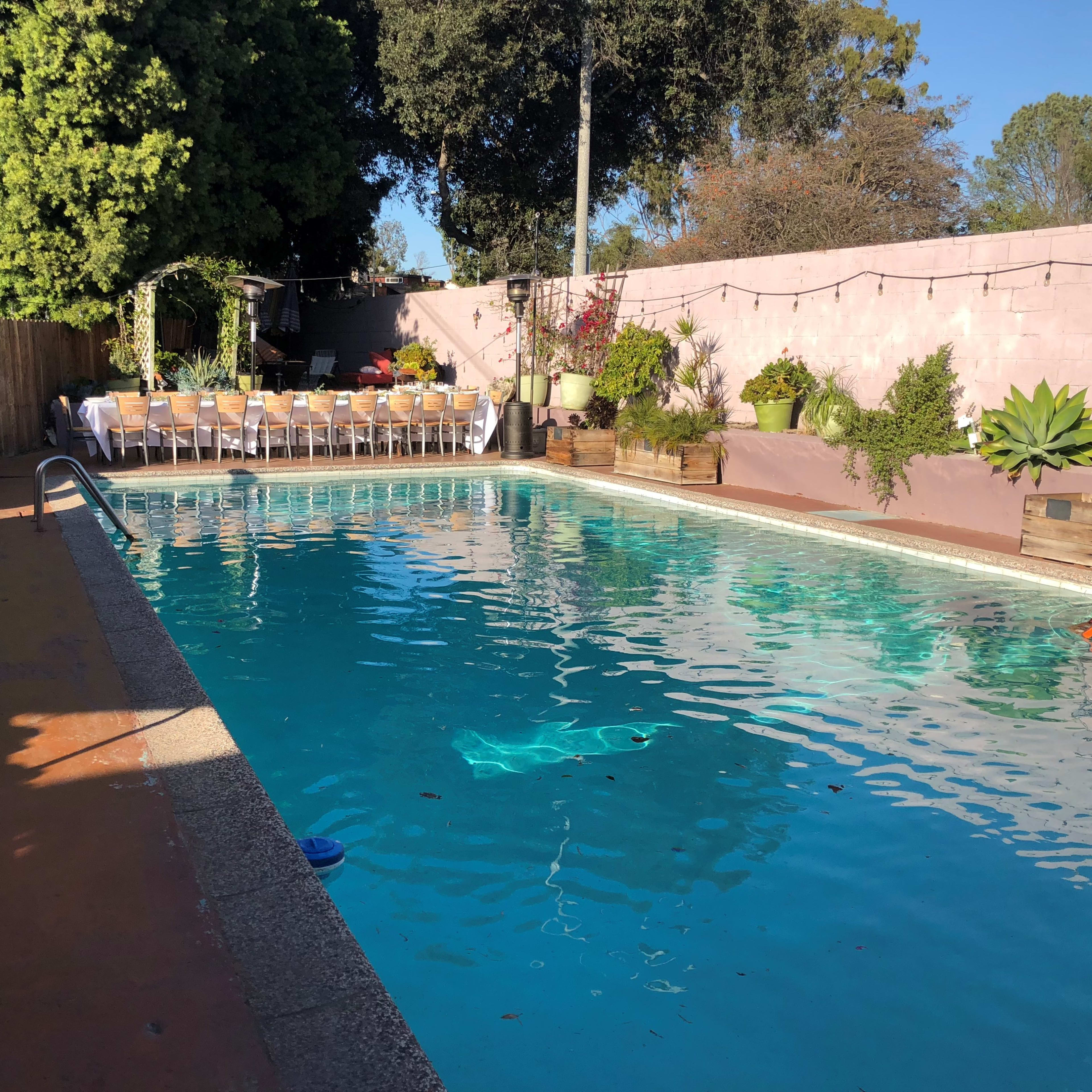 A swimming pool surrounded by a landscaped patio area with lounge chairs and a dining setup under string lights.
