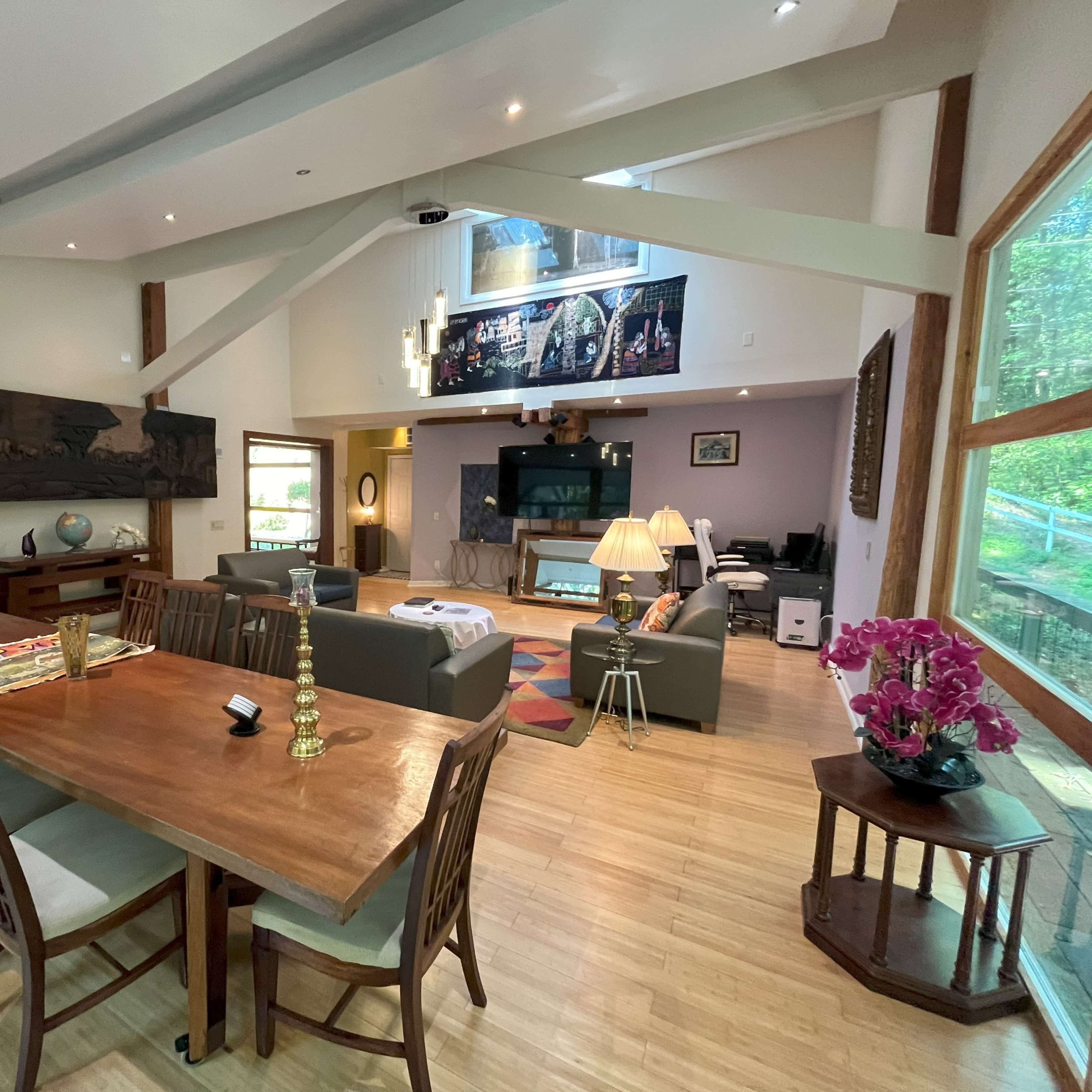 A spacious, modern living and dining area with a wooden dining table, comfortable seating, and large windows allowing natural light in.