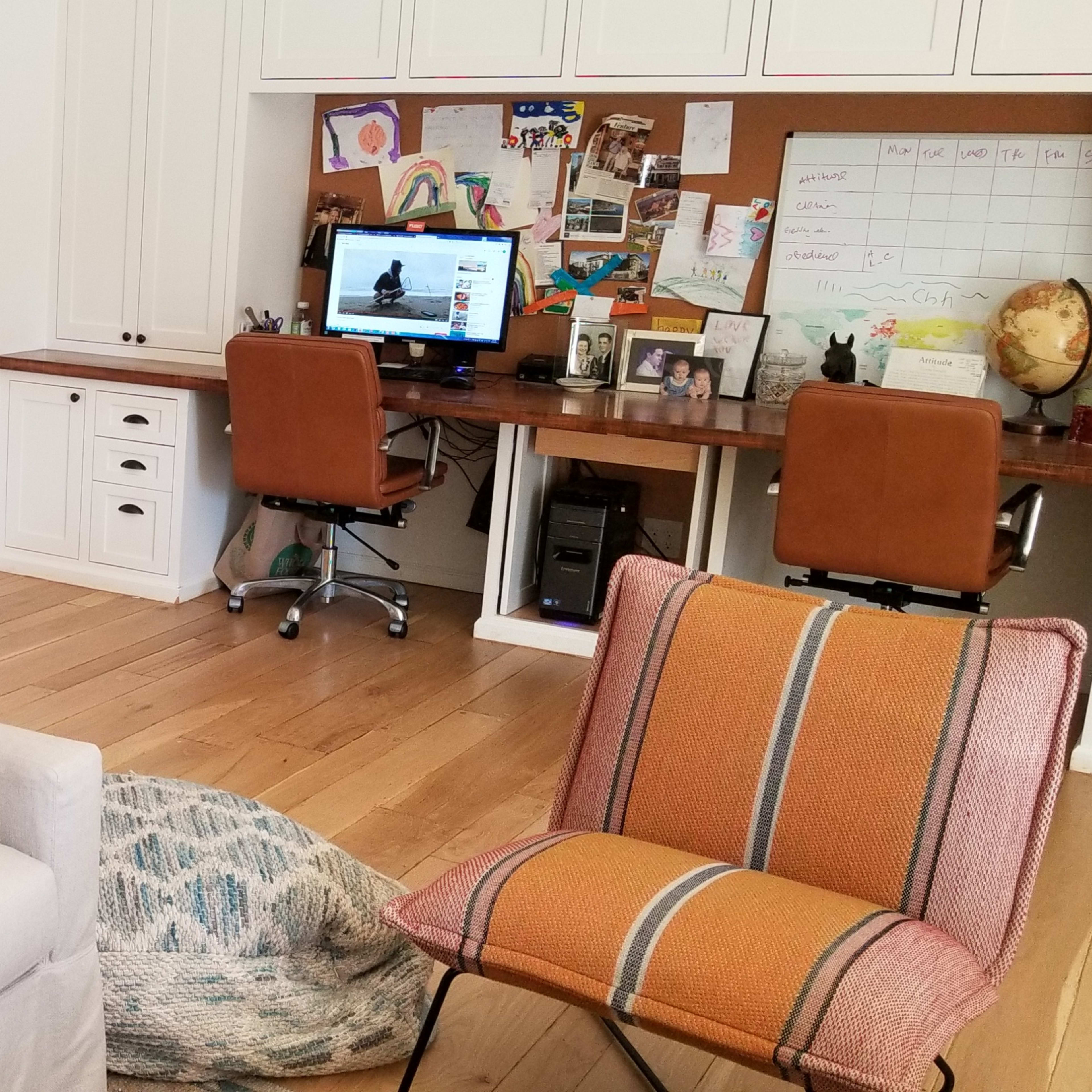 A bright, tidy room with a bookshelf filled with books on one side and a desk with a computer and a calendar on the other.