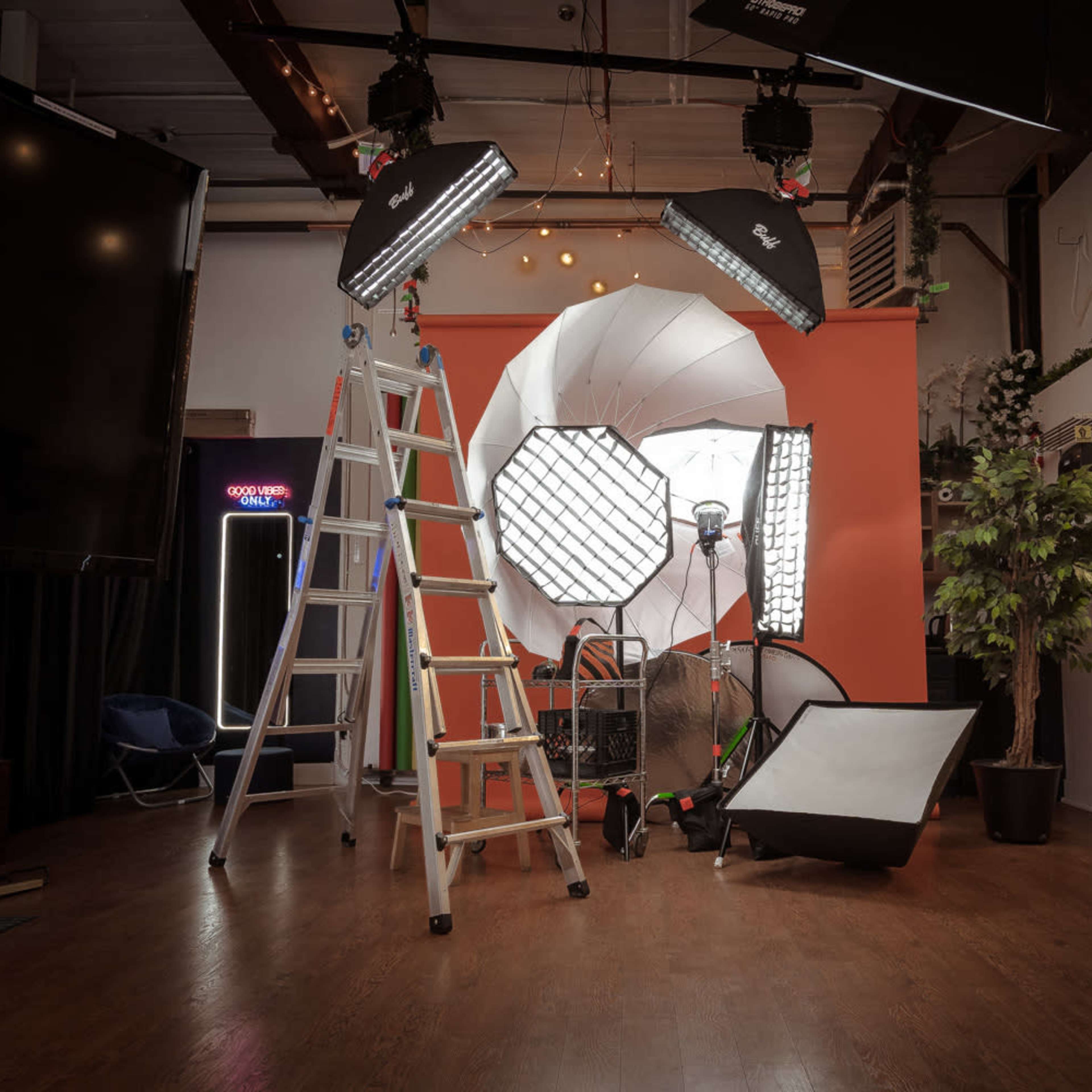 A photography studio equipped with various lighting setups, a ladder, and a backdrop.