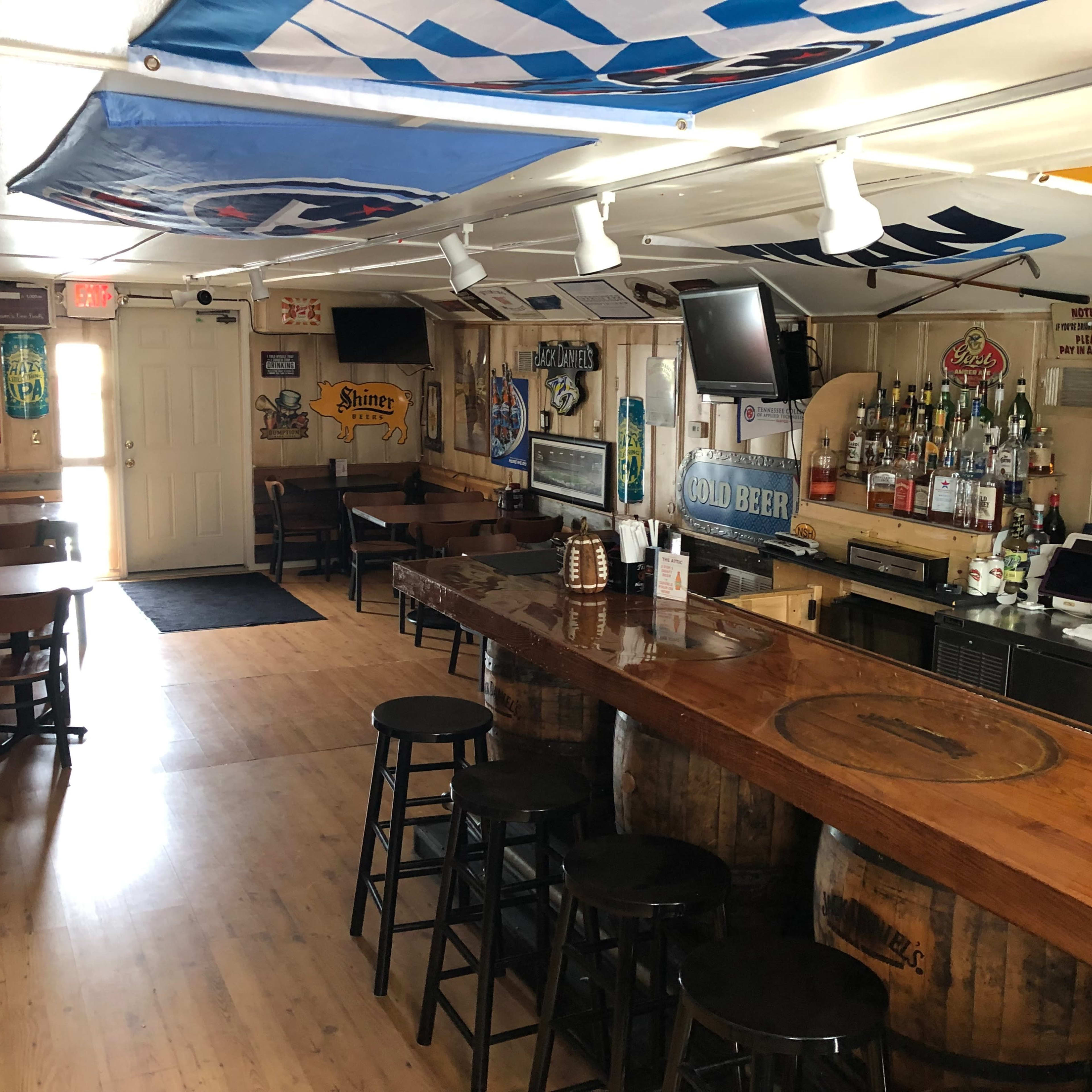 An empty bar with wooden stools, a polished counter, and various beer signs and memorabilia adorning the walls.