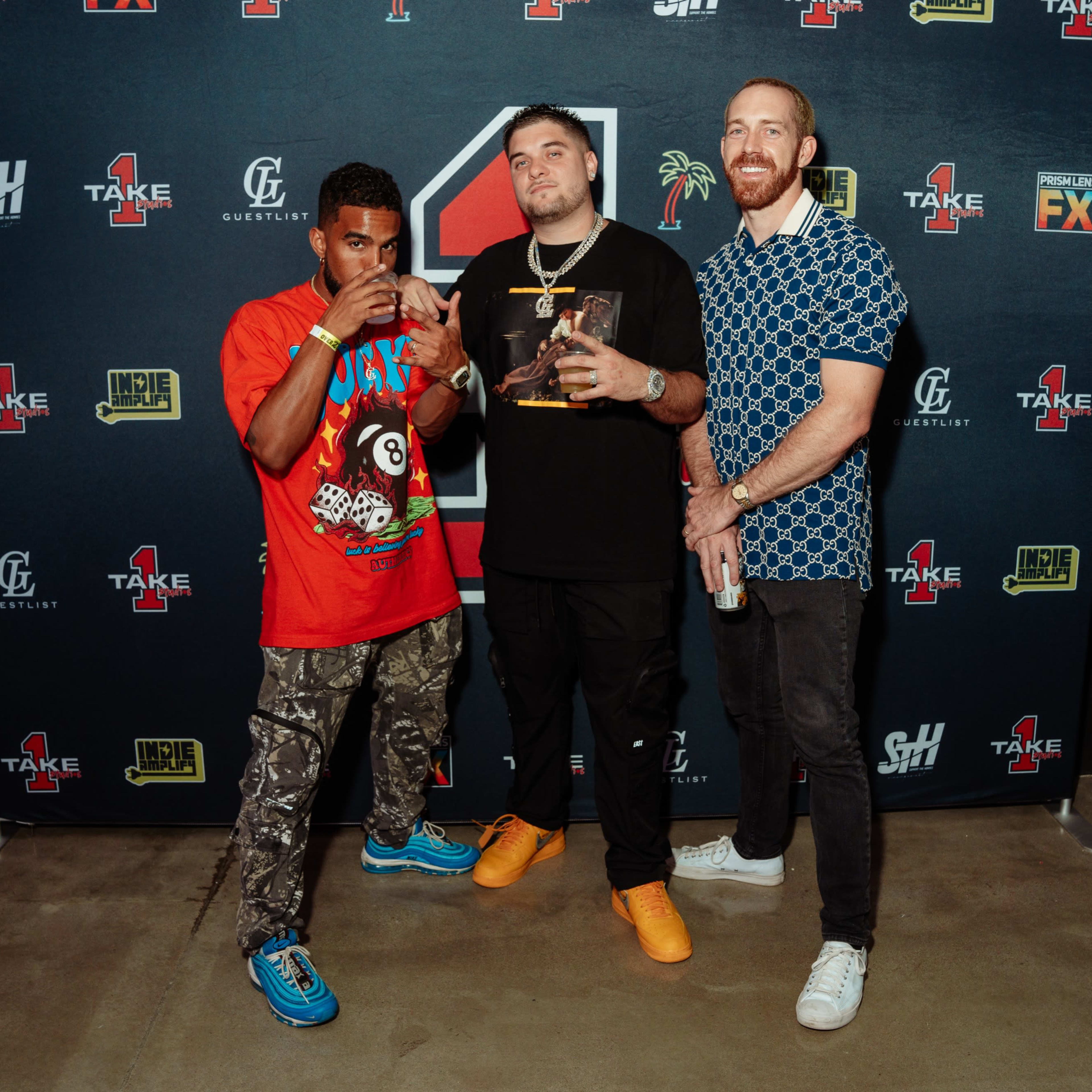 Three men pose together in front of a promotional backdrop at an event.