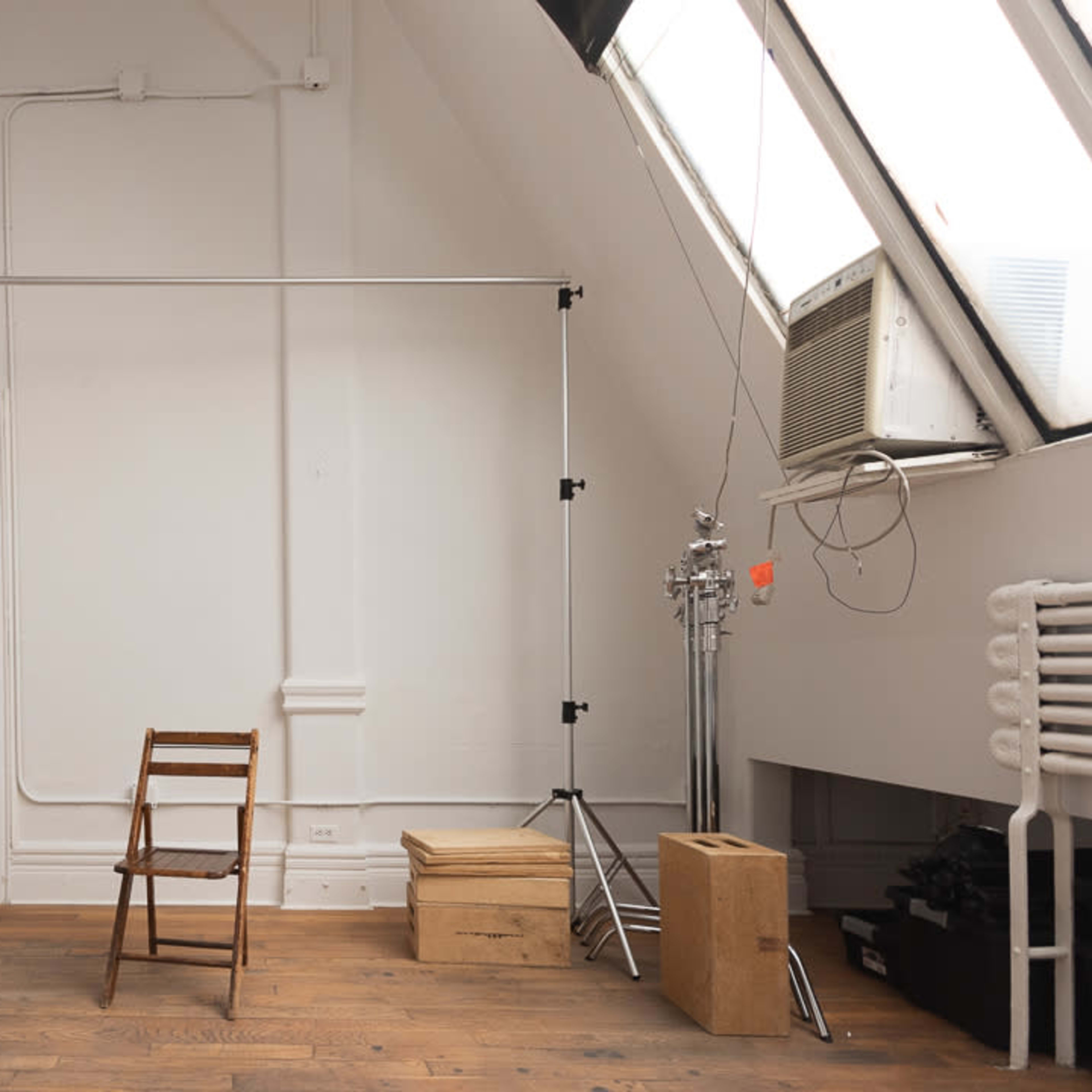 A sparsely furnished room with a wooden chair, a backdrop stand, and some wooden boxes against the walls.