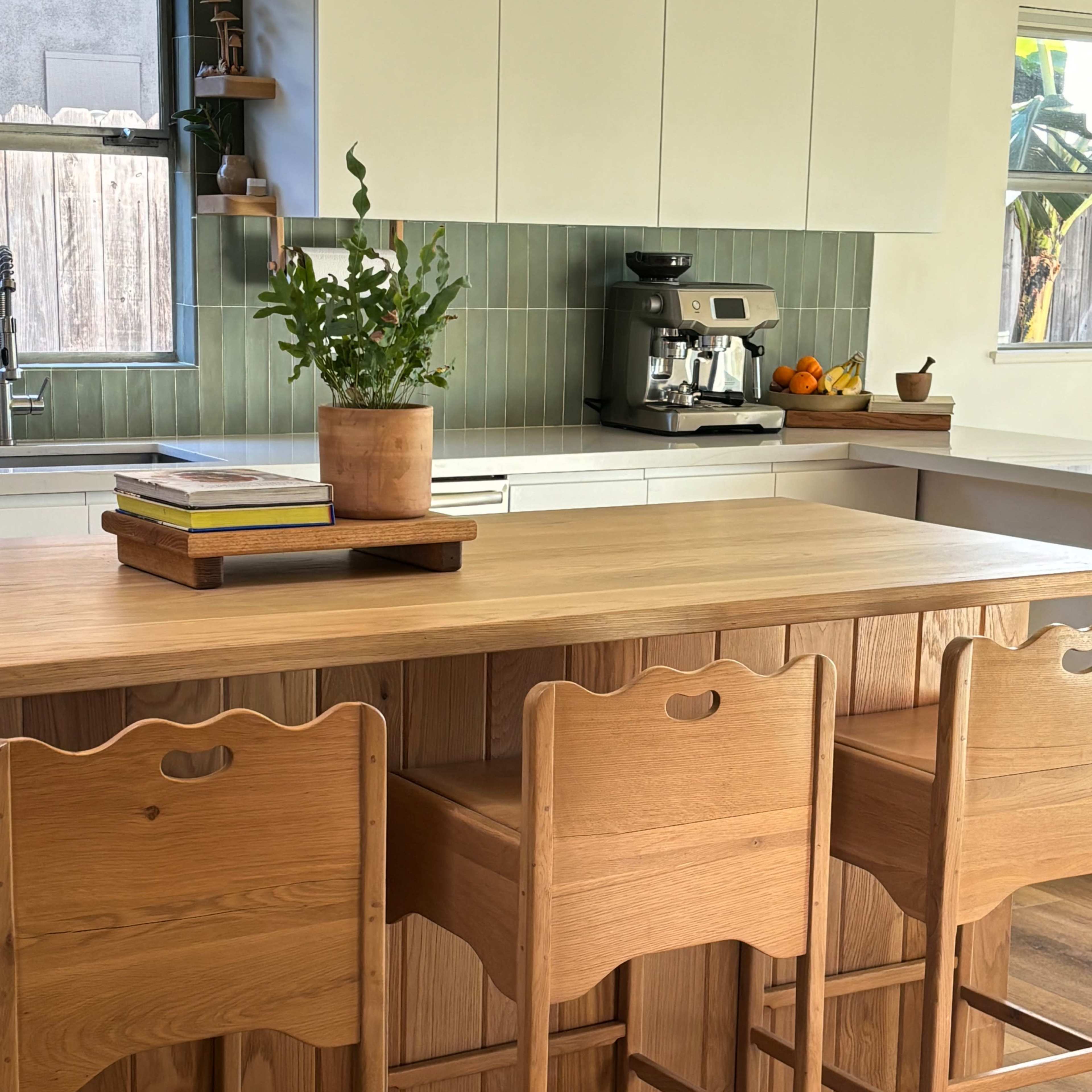 A modern kitchen features a wooden island with three stools, a plant in a pot, and a coffee maker on the counter.