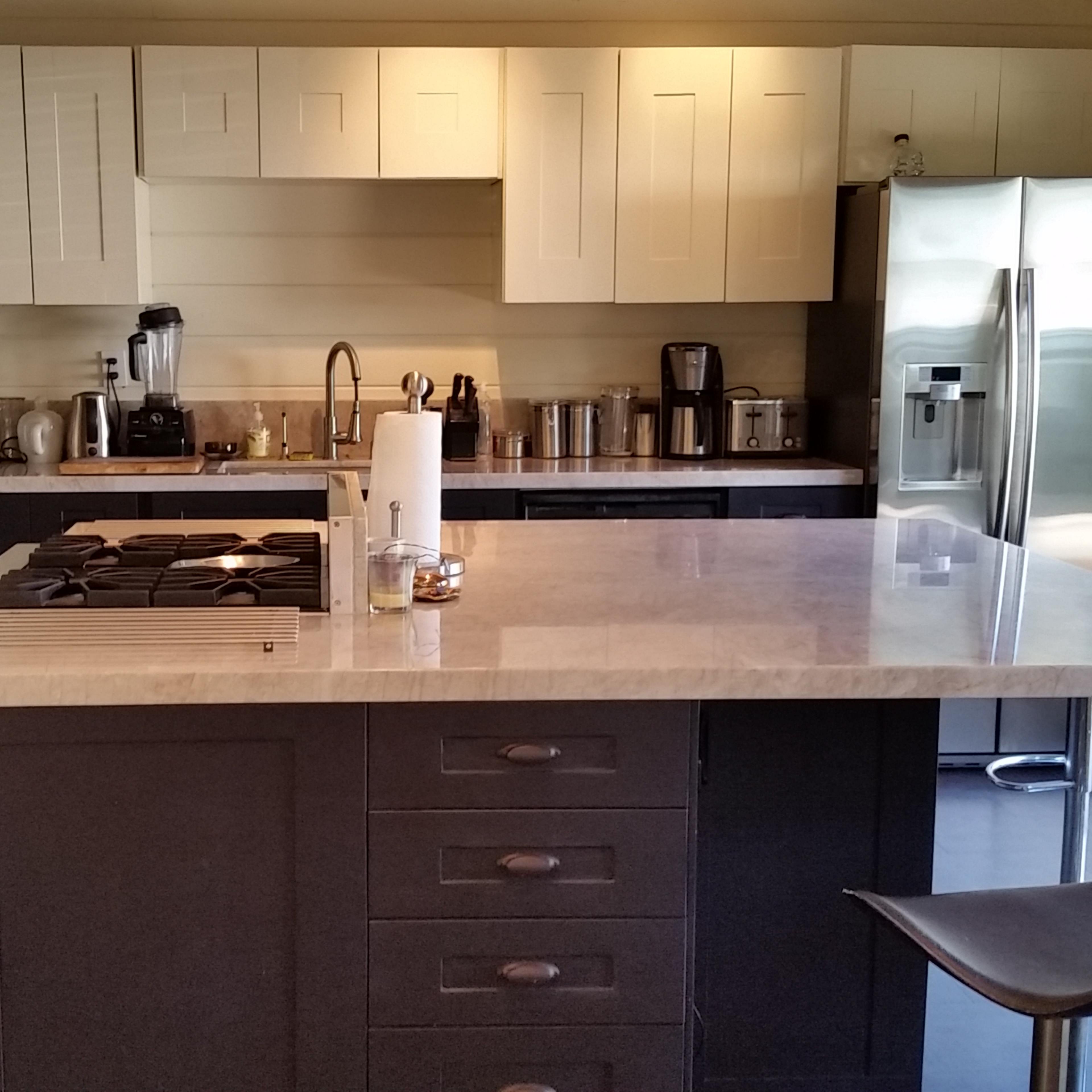 A modern kitchen features a central island with a stovetop, stainless steel appliances, and various countertop appliances against a backdrop of cabinetry.