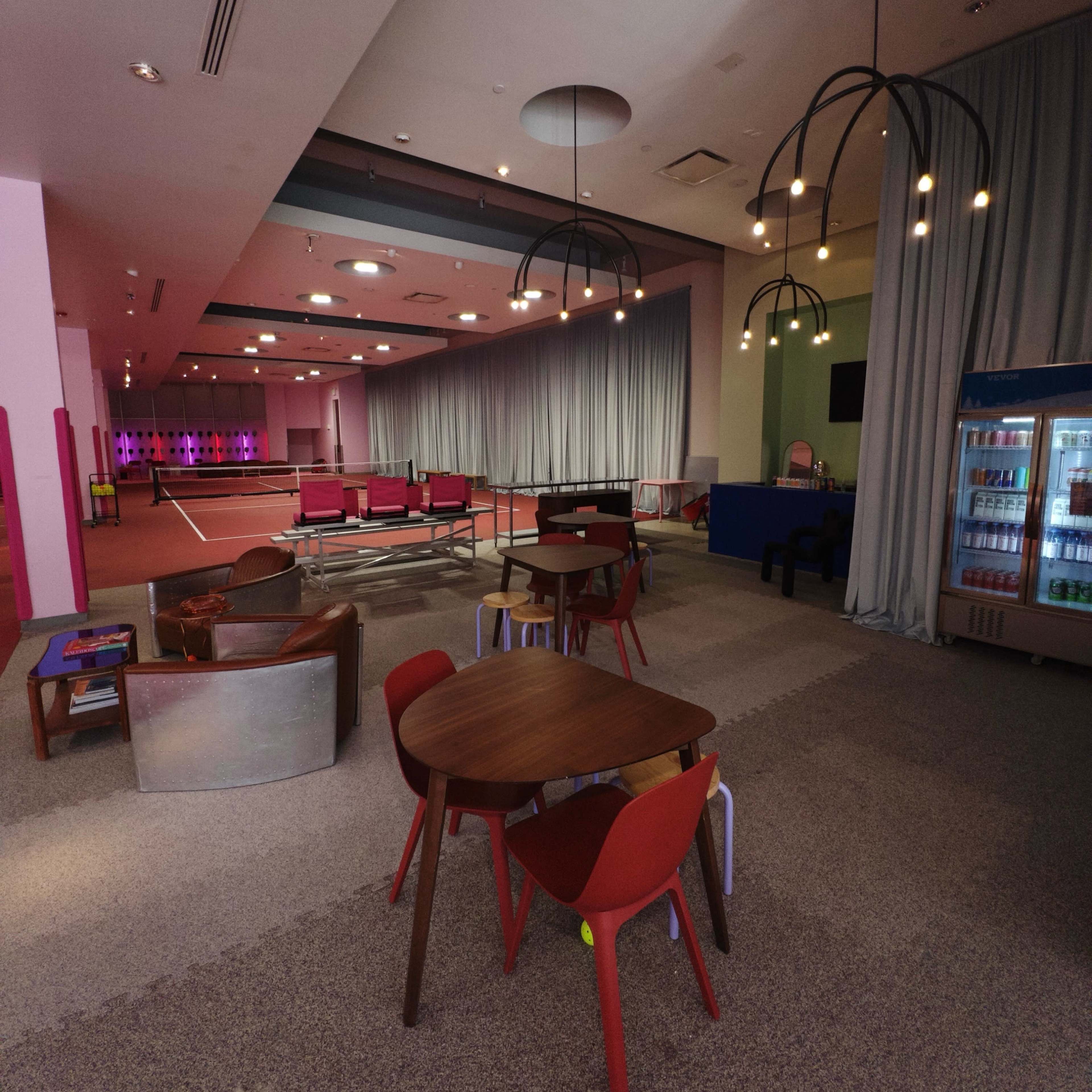 A modern lounge area with colorful furniture, including tables and chairs, and illuminated features in a spacious, partially curtained space.