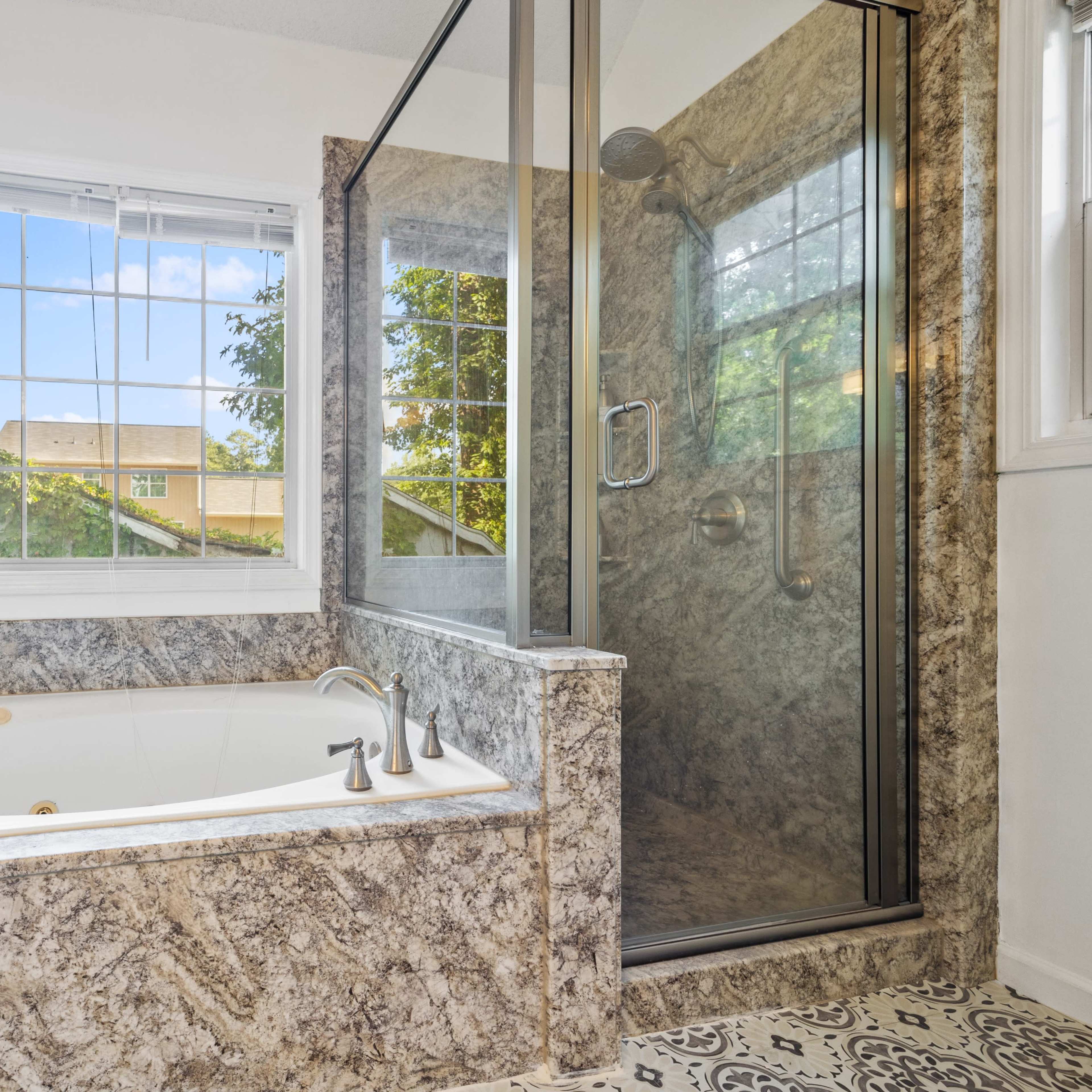 A modern bathroom with a freestanding soaking tub alongside a glass-enclosed shower, set against a backdrop of large windows.