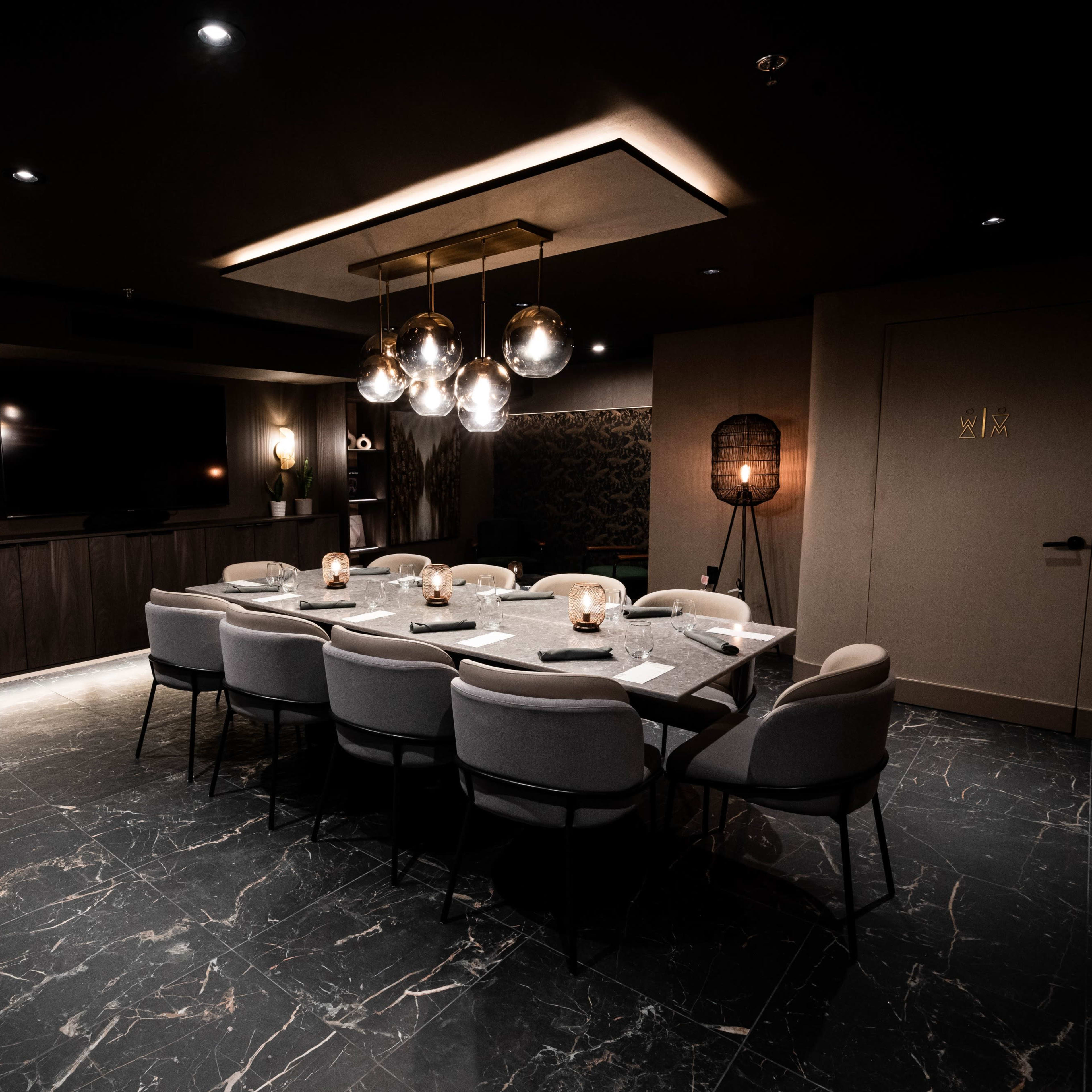 A sleek conference room features a large table surrounded by chairs, illuminated by modern pendant lights.