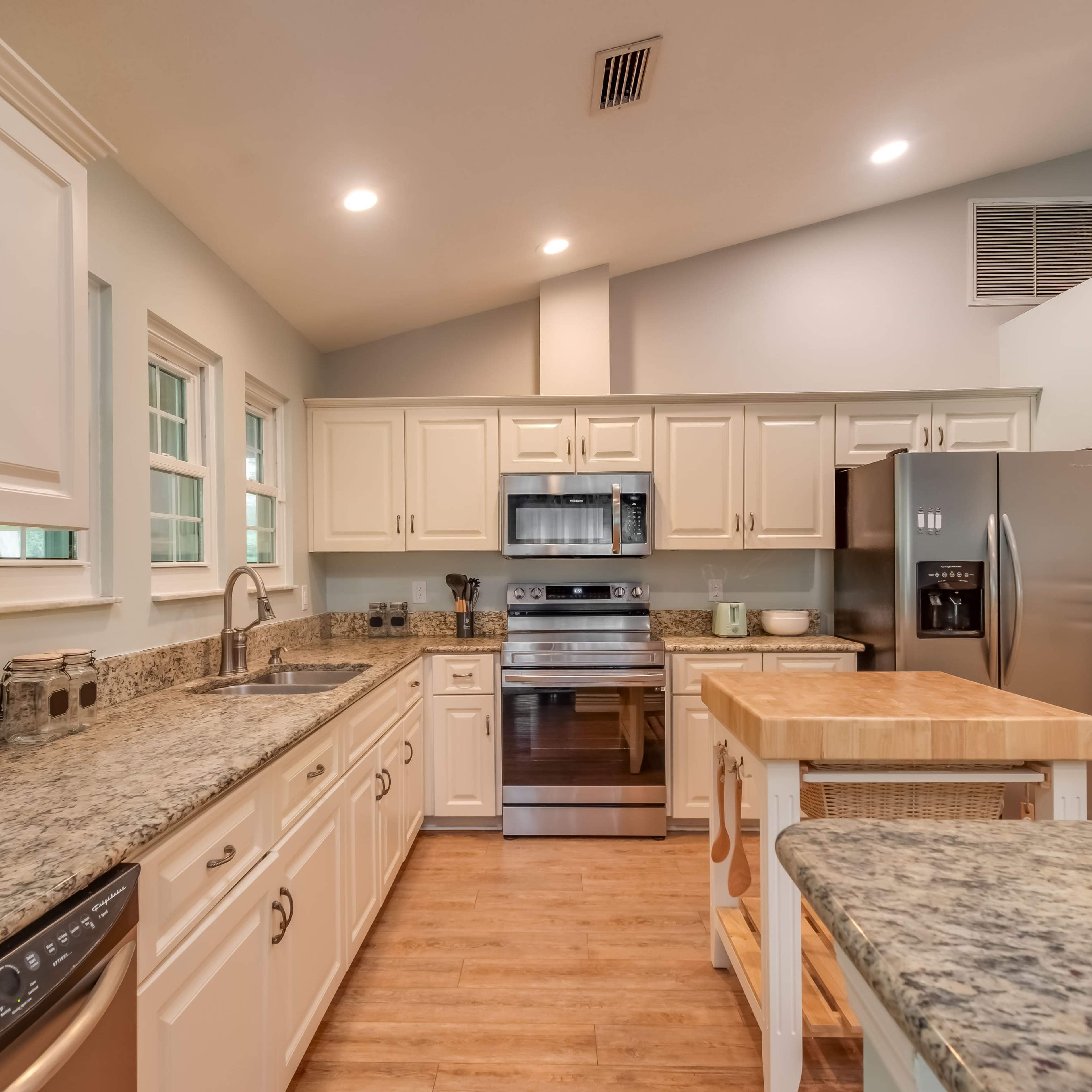A modern kitchen featuring white cabinets, granite countertops, stainless steel appliances, and a wooden island in the center.