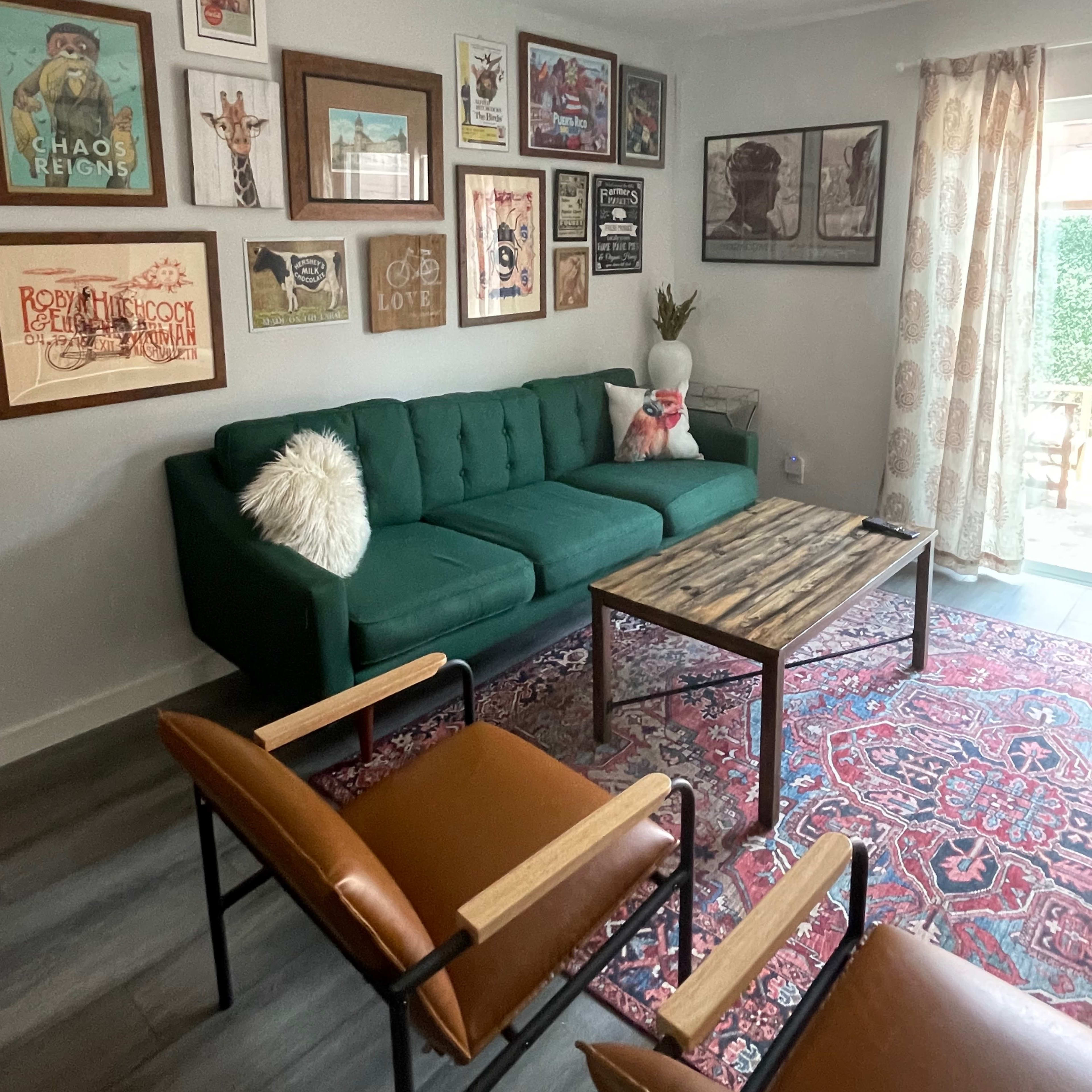 A cozy living room features a green sofa, a wooden coffee table, and artwork displayed on the walls, with a patterned rug underfoot.