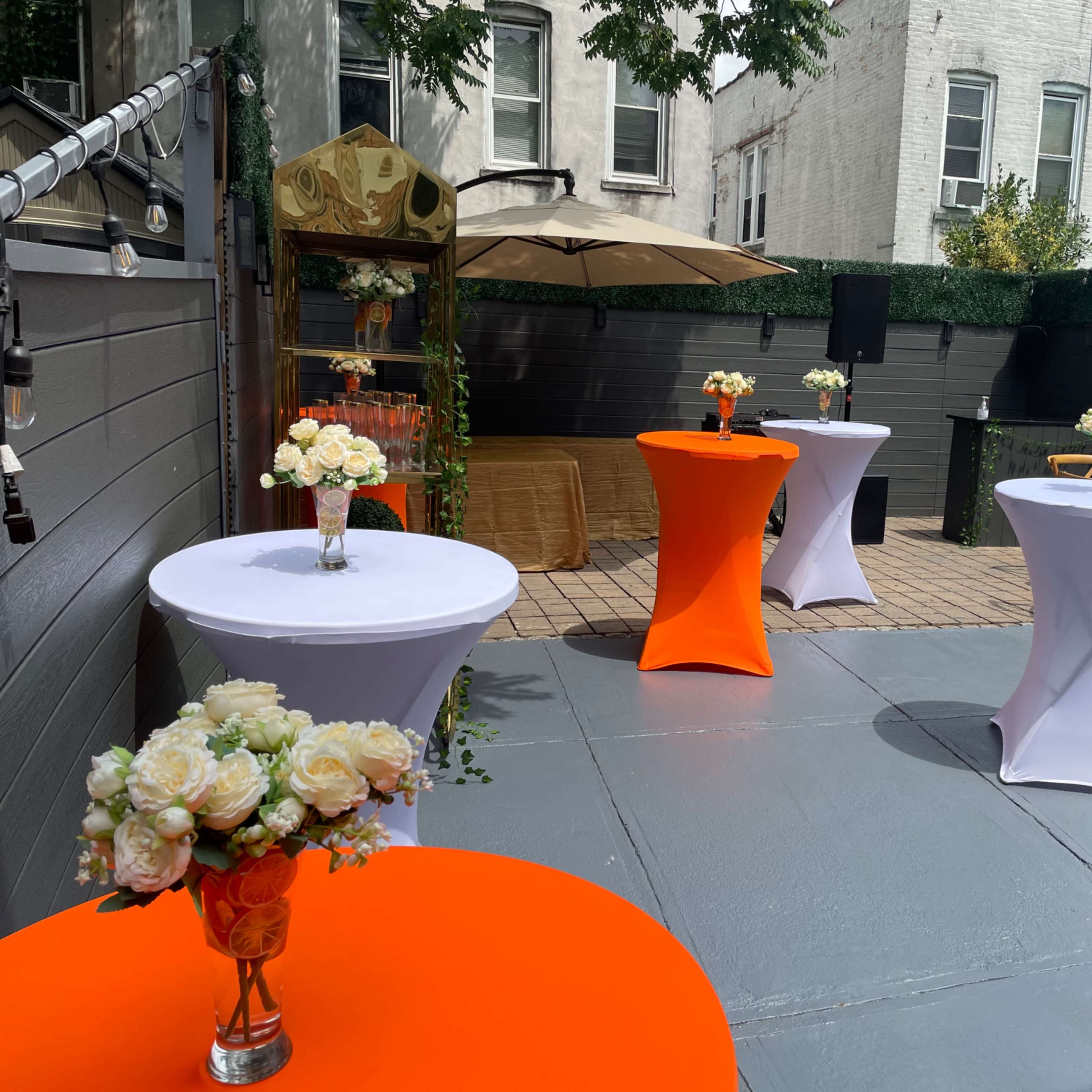 The outdoor event space features several cocktail tables with vibrant tablecloths and floral centerpieces arranged around a paved area.