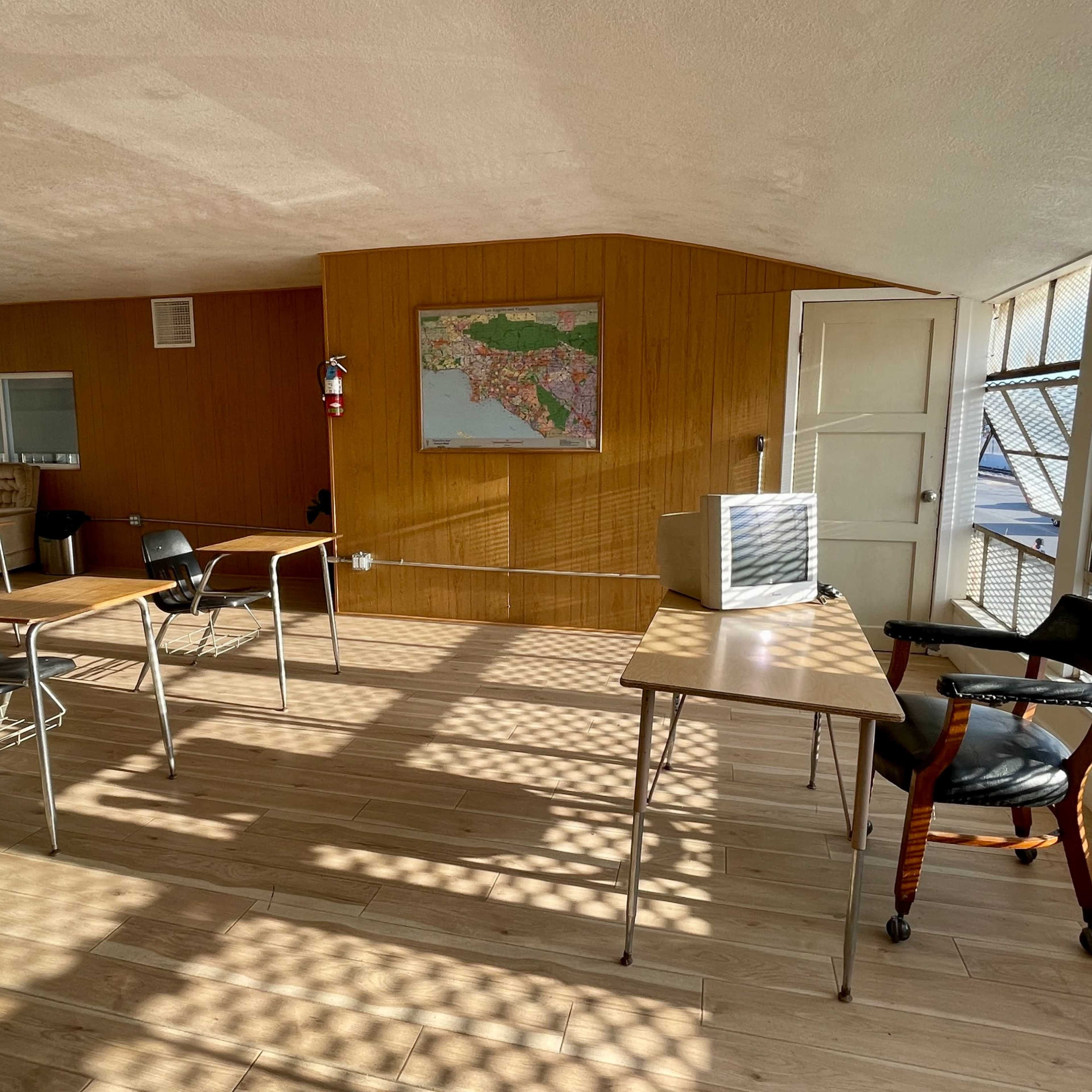 An empty classroom with wooden flooring, several desks, and a map of Florida on the wall.