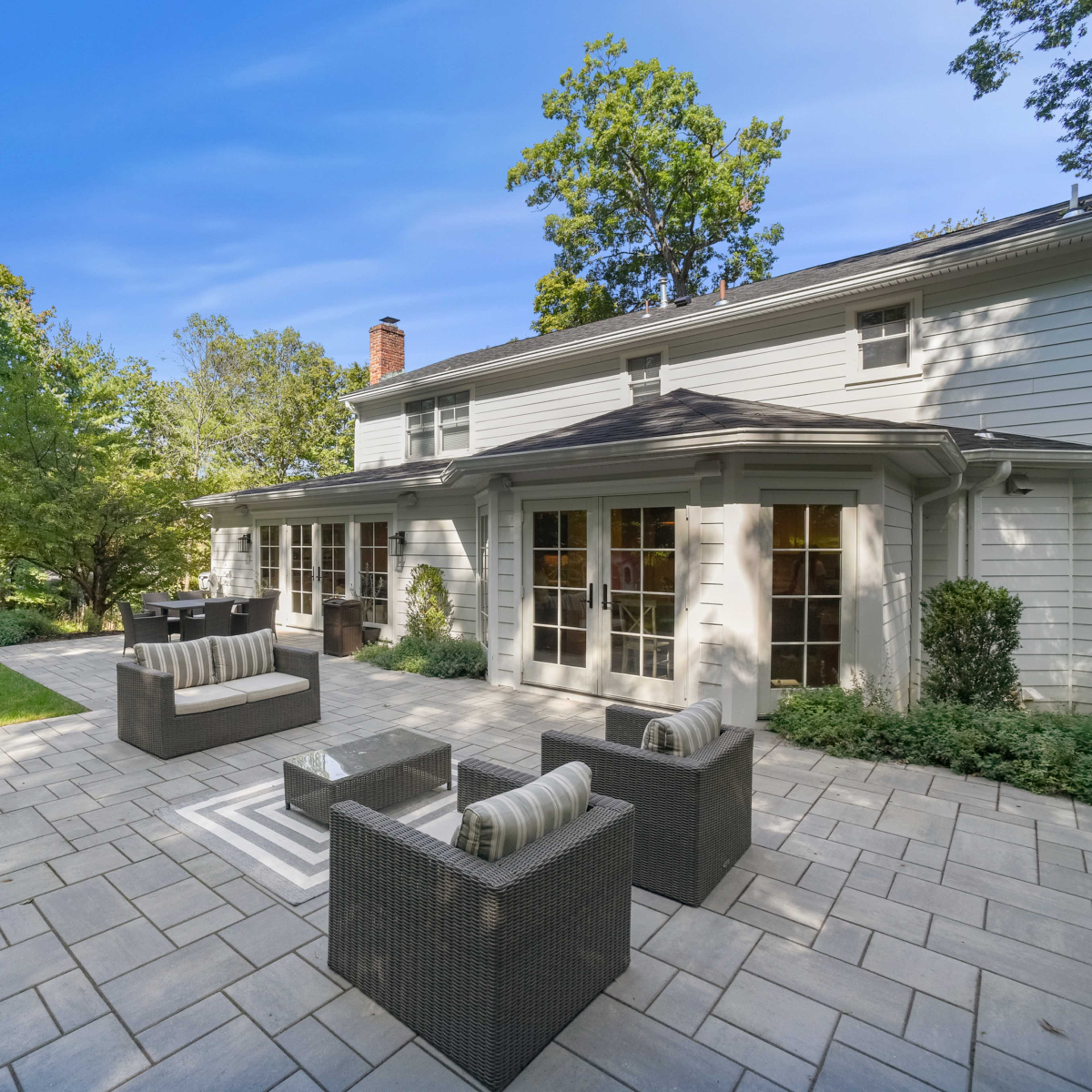 A patio area with modern outdoor furniture set against a backdrop of a well-maintained lawn and trees.