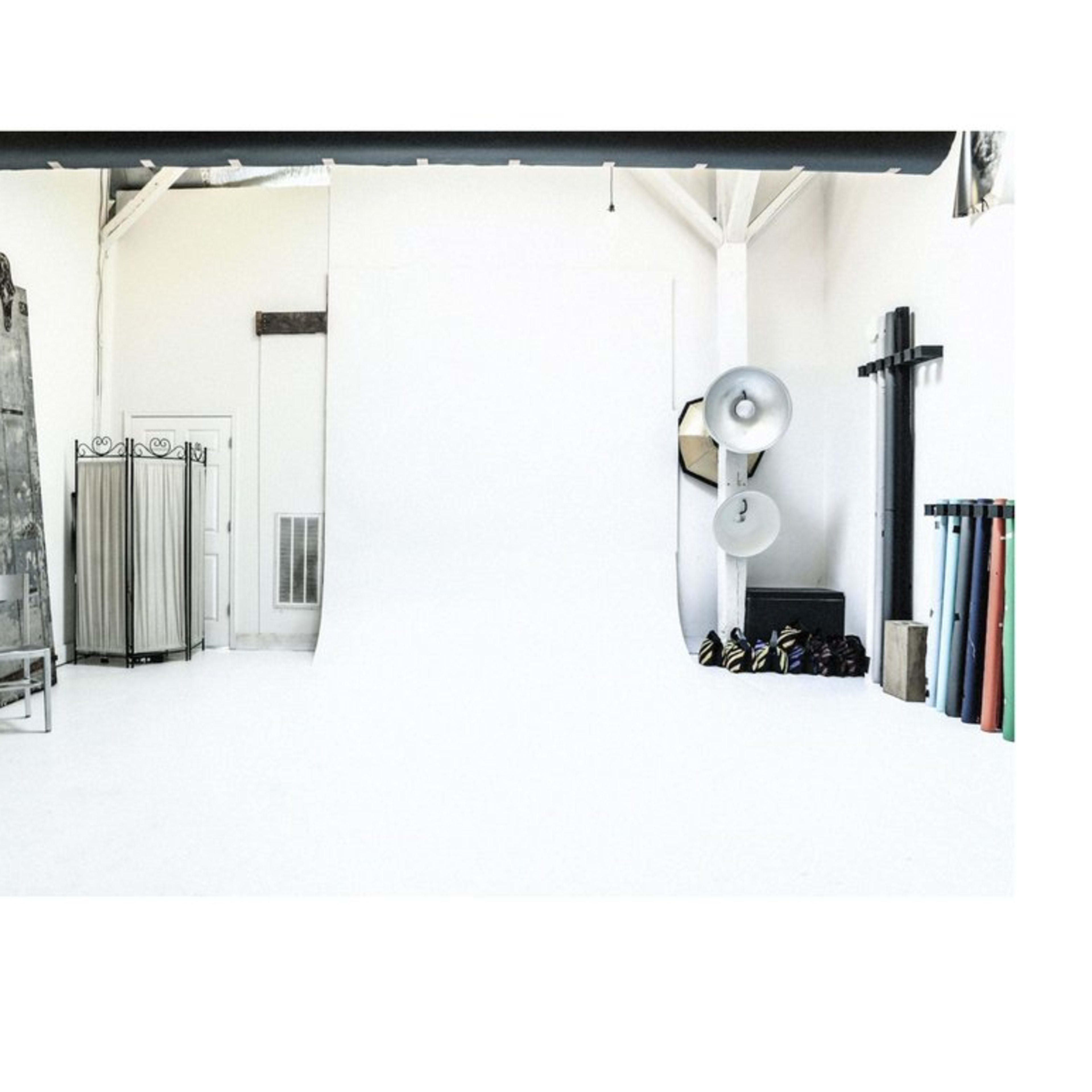A spacious, minimalist photography studio with a white backdrop and various equipment along the walls.