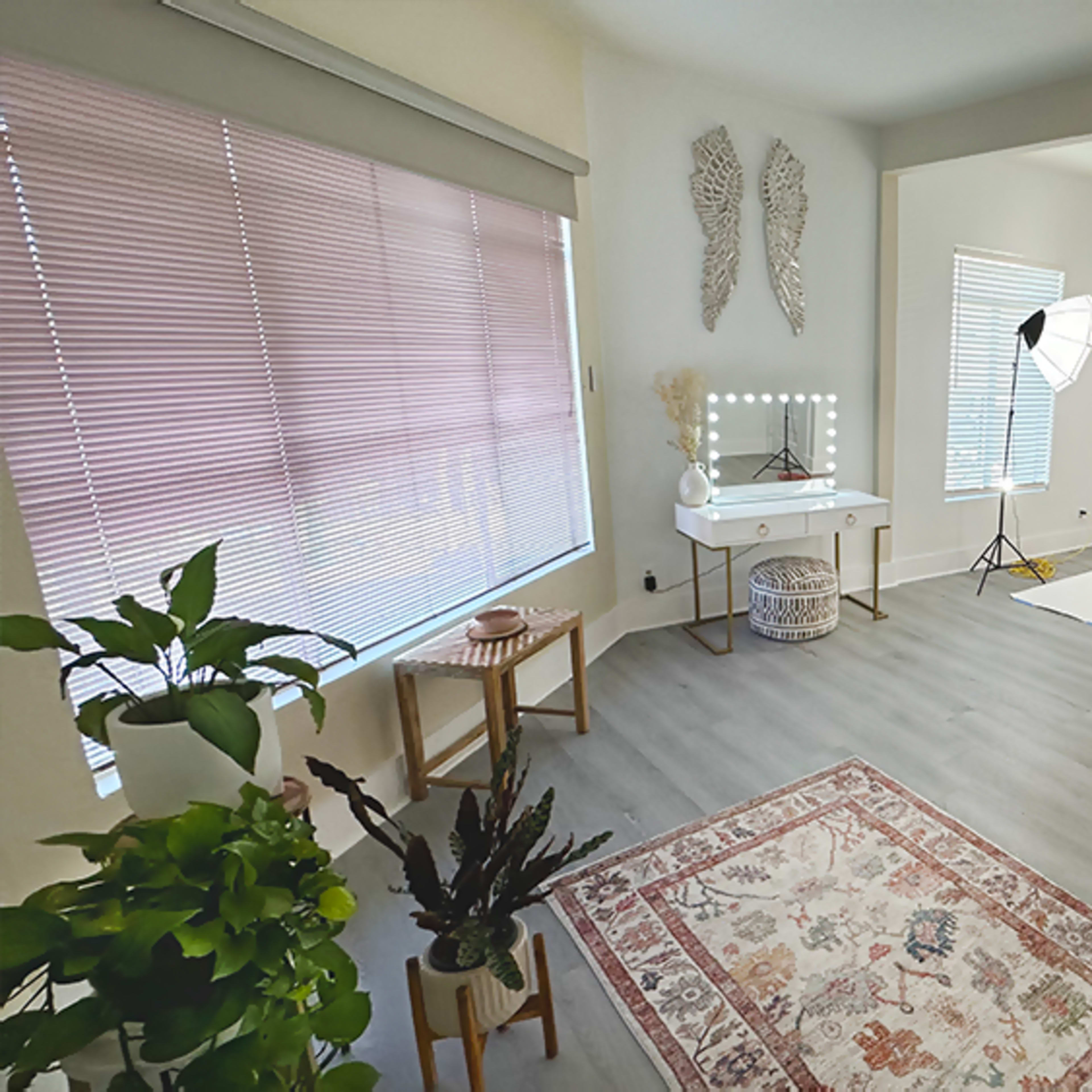A well-lit studio space with a white backdrop, professional lighting equipment, a vanity table, a small plant, and a decorative rug on the floor.
