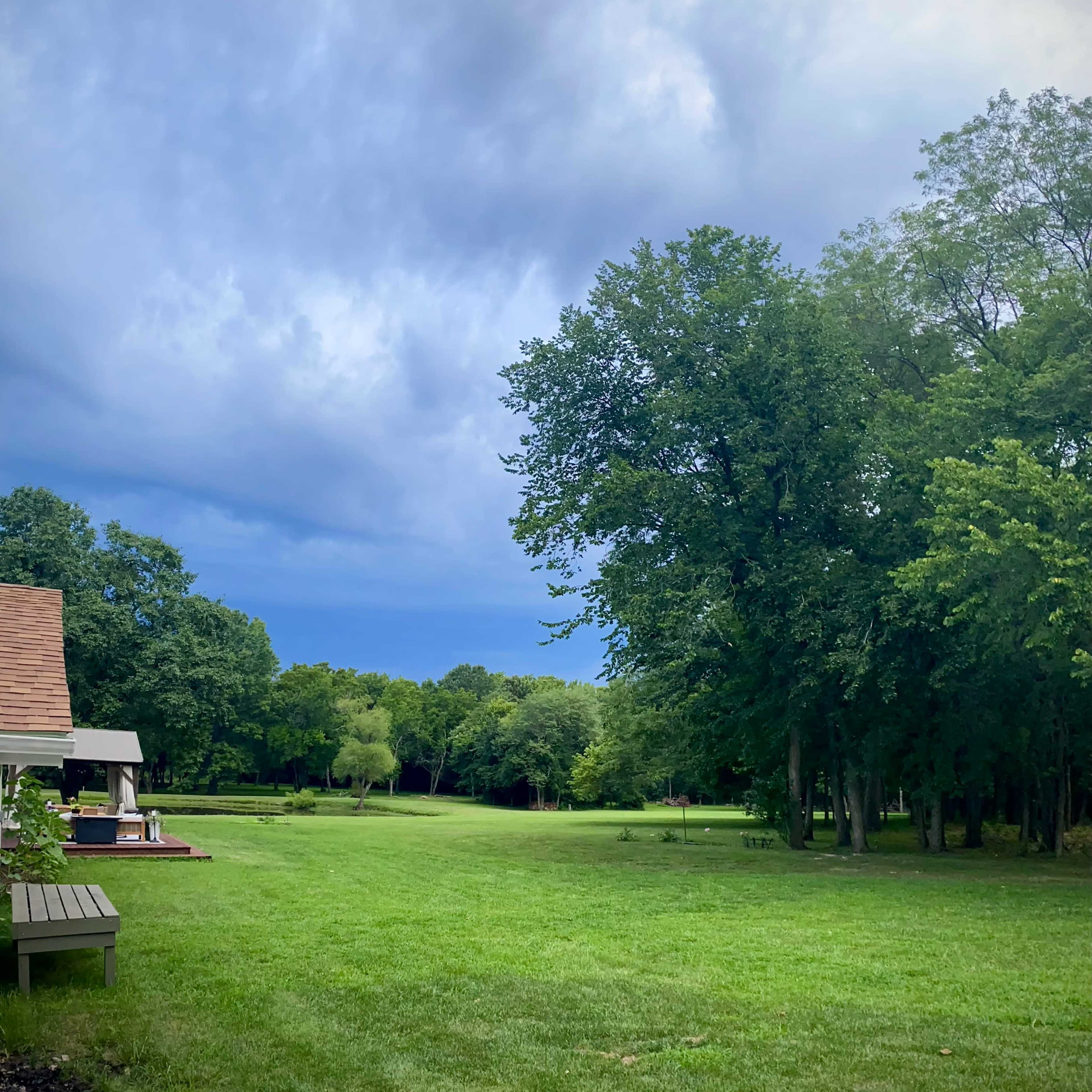 A wide green lawn is bordered by trees under a mostly cloudy sky.