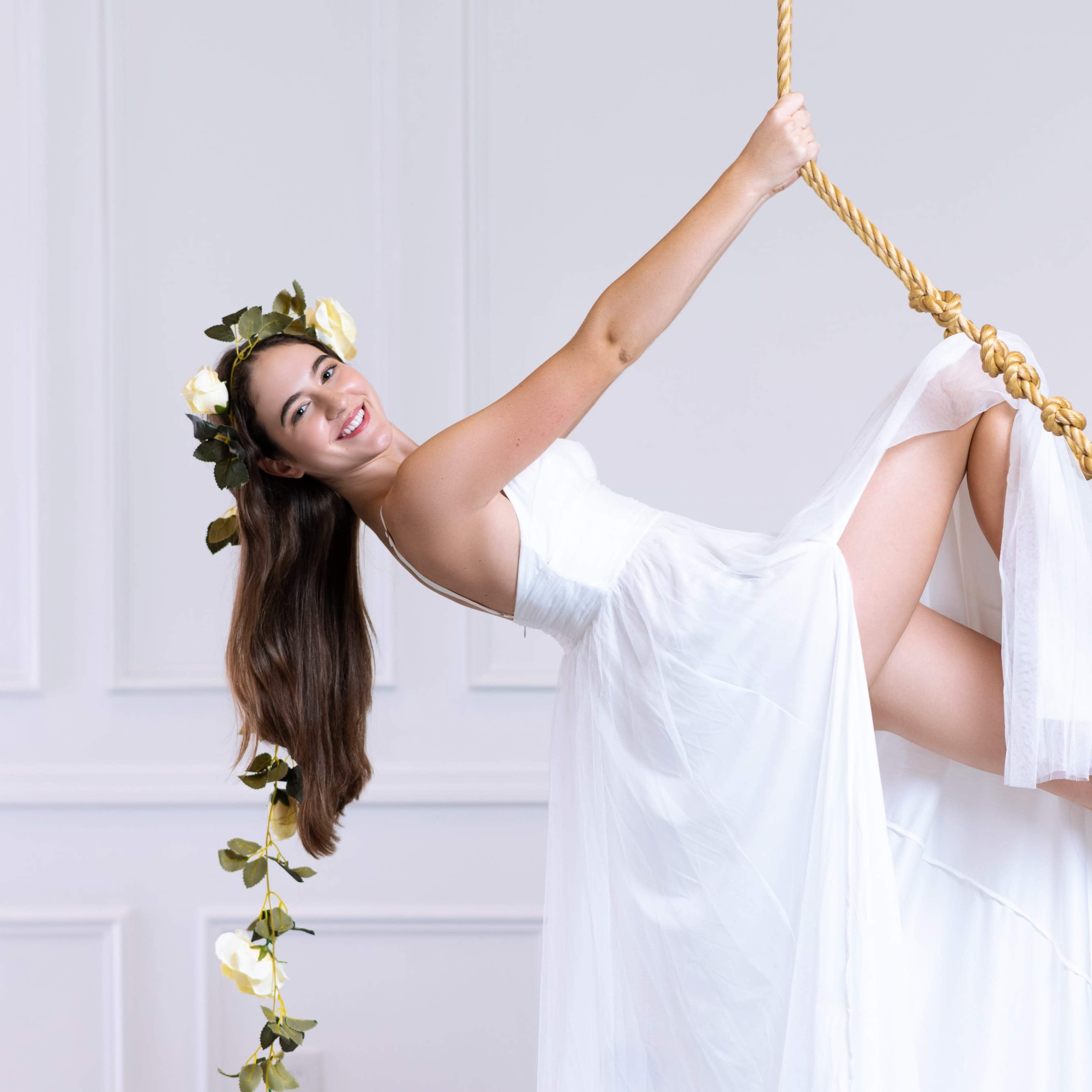 A woman in a white dress swings on a rope in a bright, decorated interior.