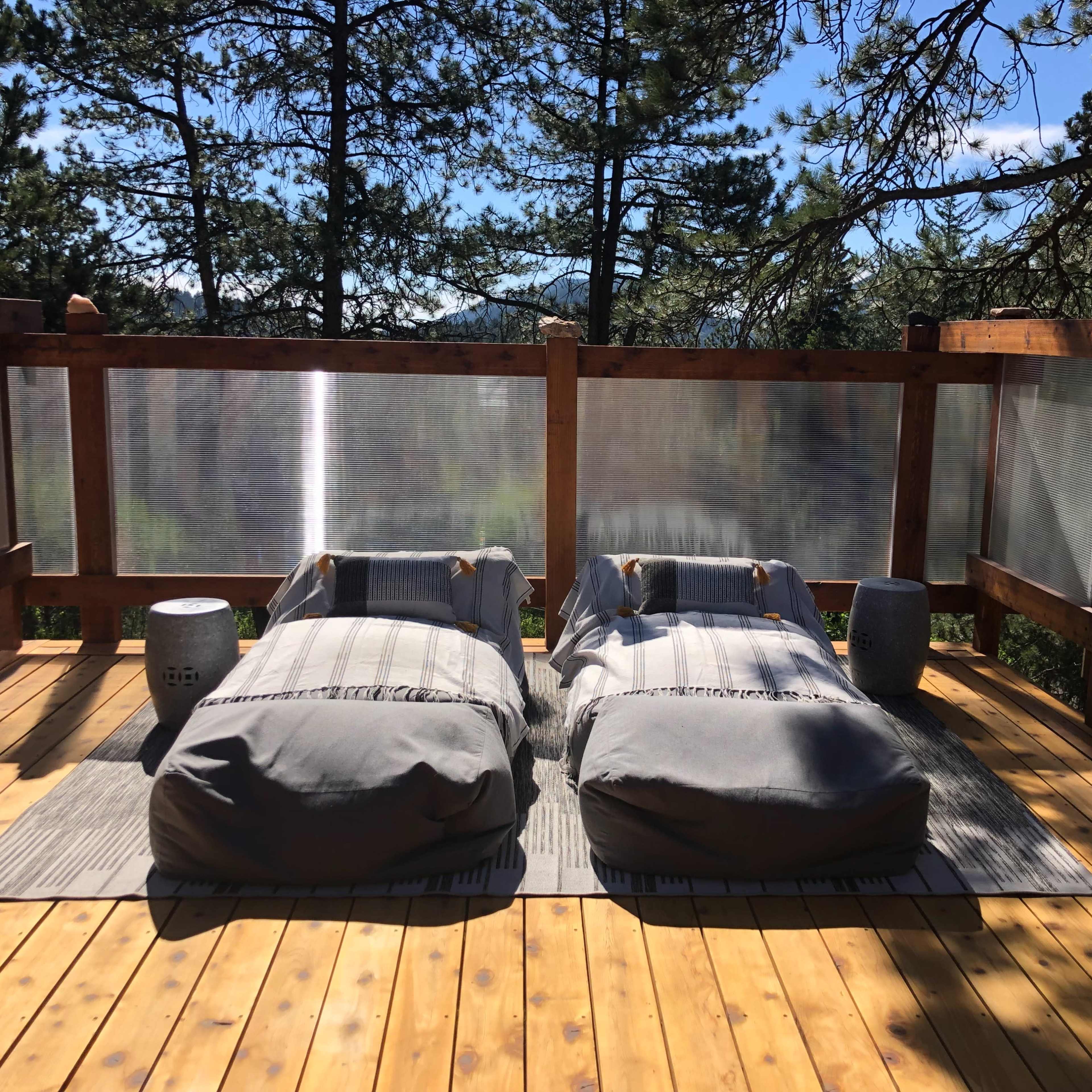 Two outdoor lounge beds arranged on a wooden deck surrounded by trees.