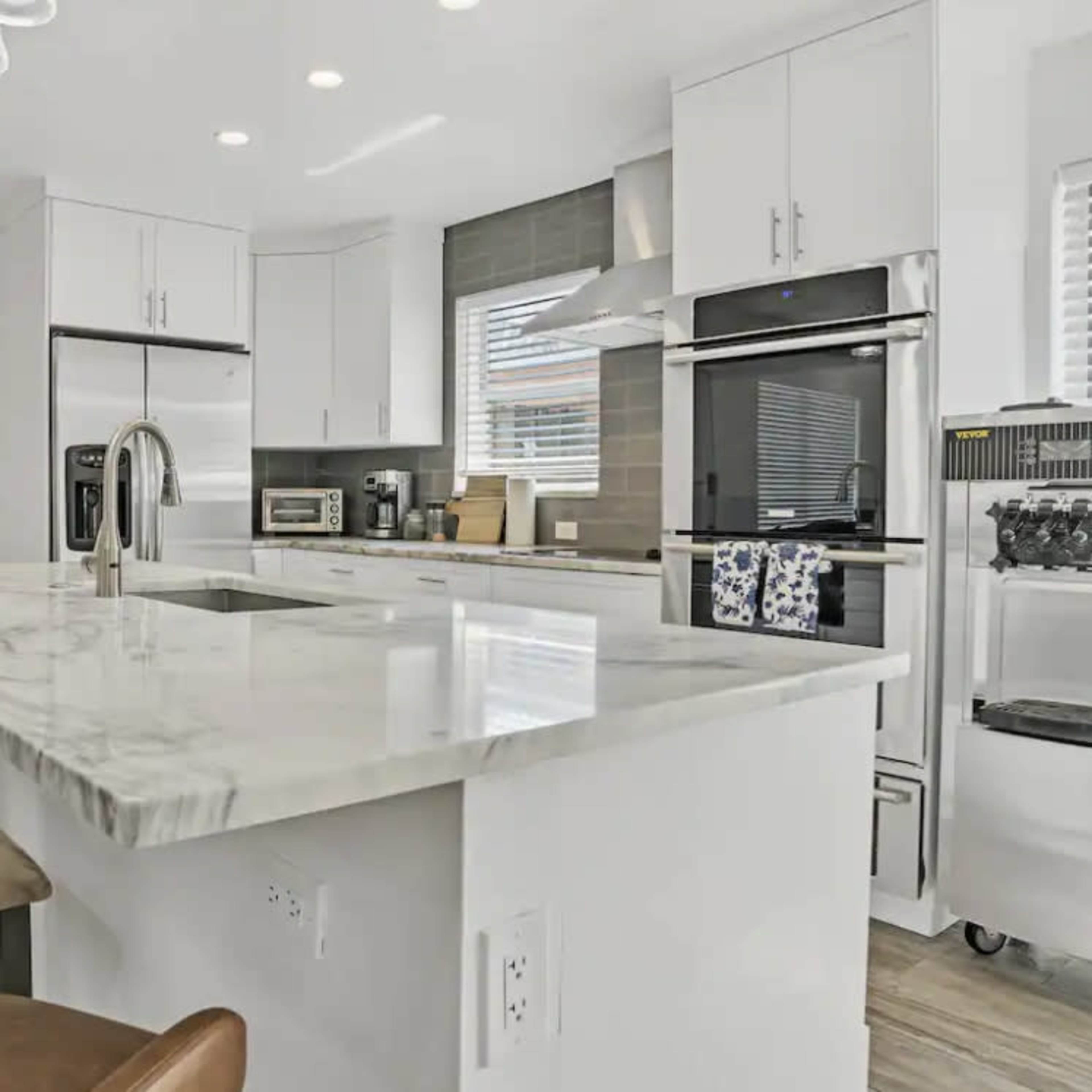 A modern kitchen with a marble countertop island, stainless steel appliances, and sleek white cabinetry.