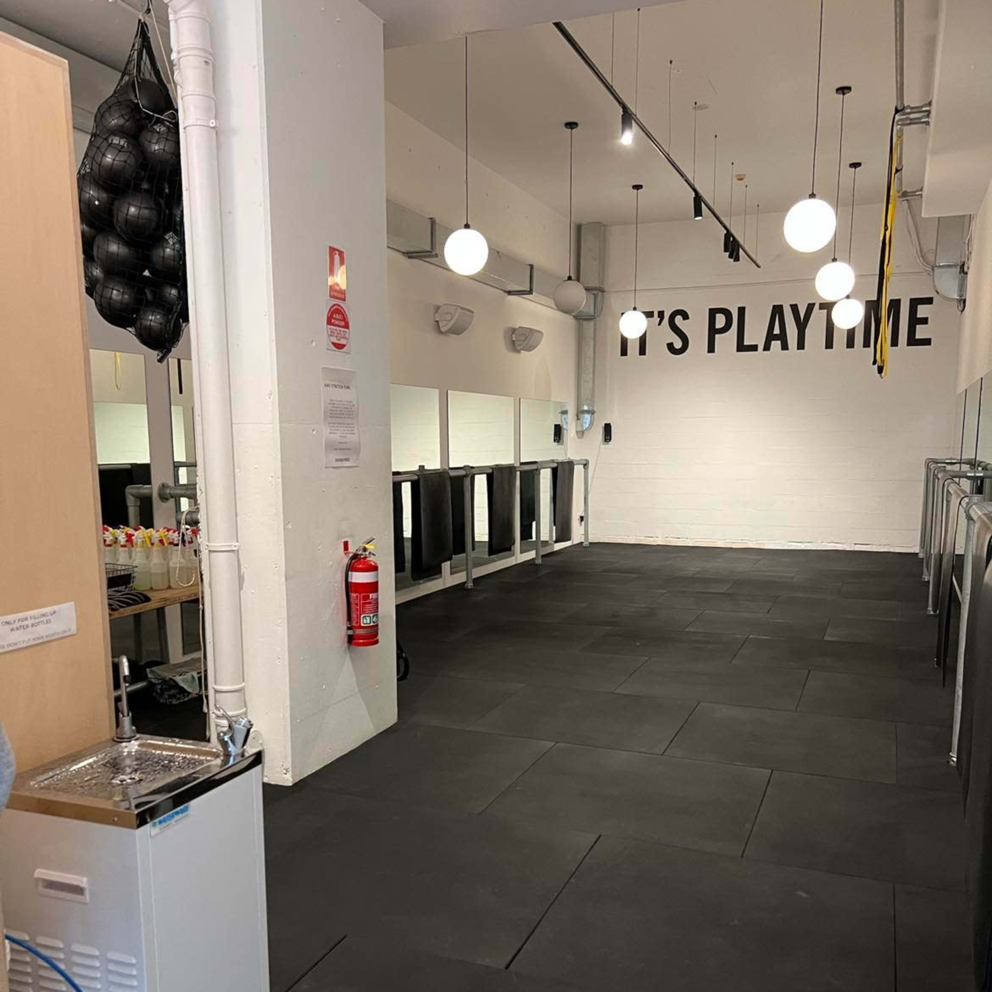 A spacious indoor area with black rubber flooring, ceiling lights, and a wall featuring the text "IT'S PLAYTIME."