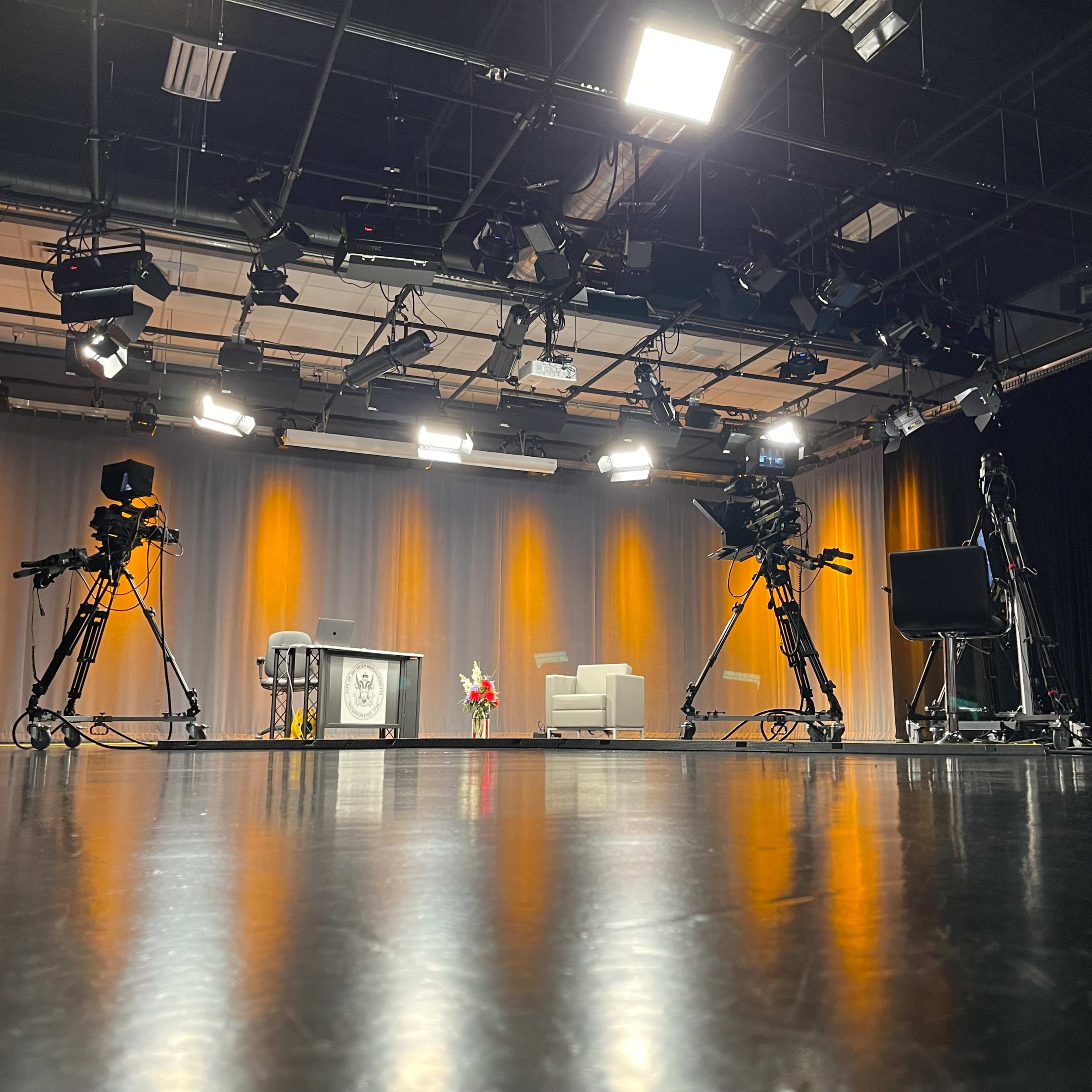 A television studio equipped with cameras, a set featuring a couch and table, and multiple lighting fixtures overhead.