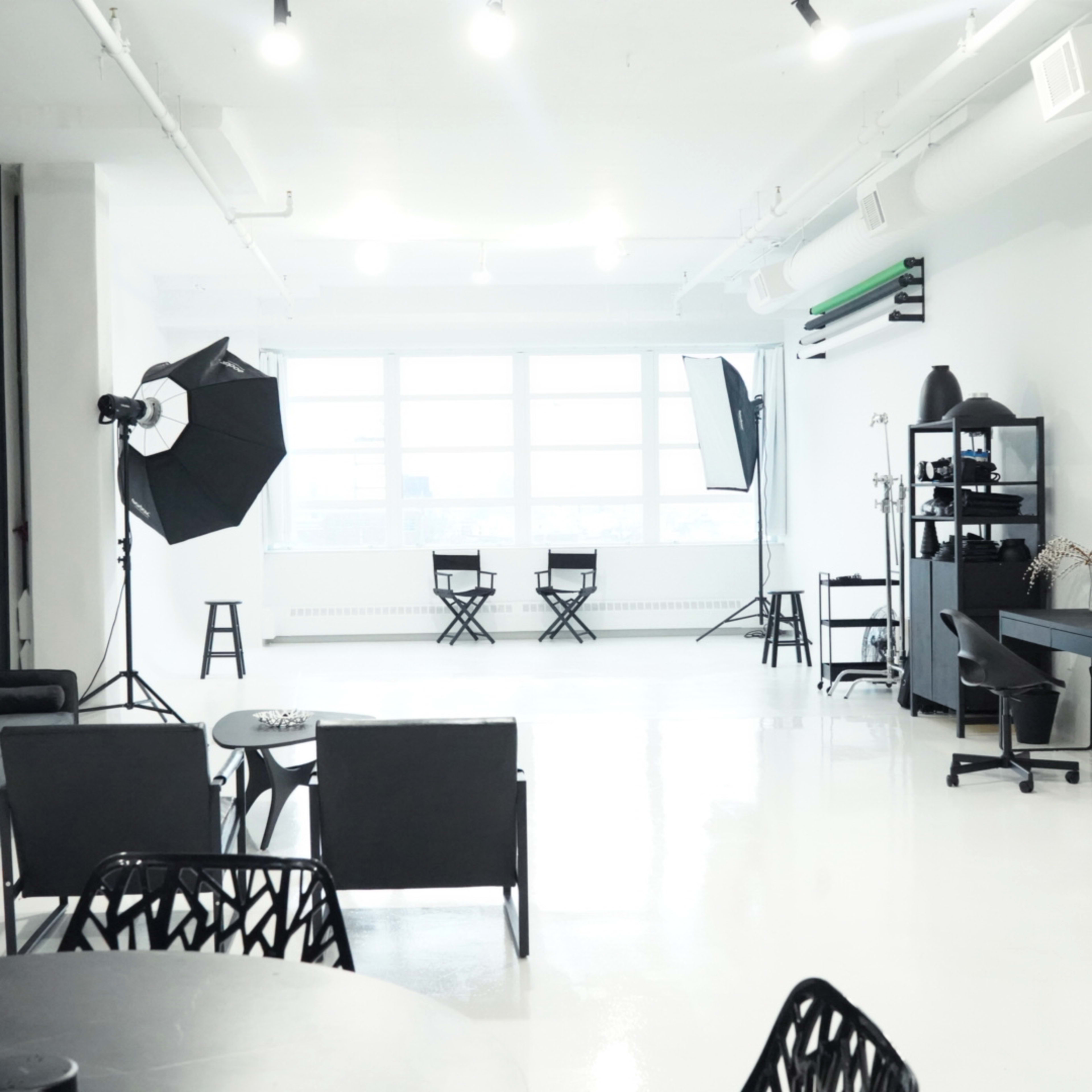 A spacious, modern studio with a bright, white floor, black accent walls, and various photography equipment arranged throughout.