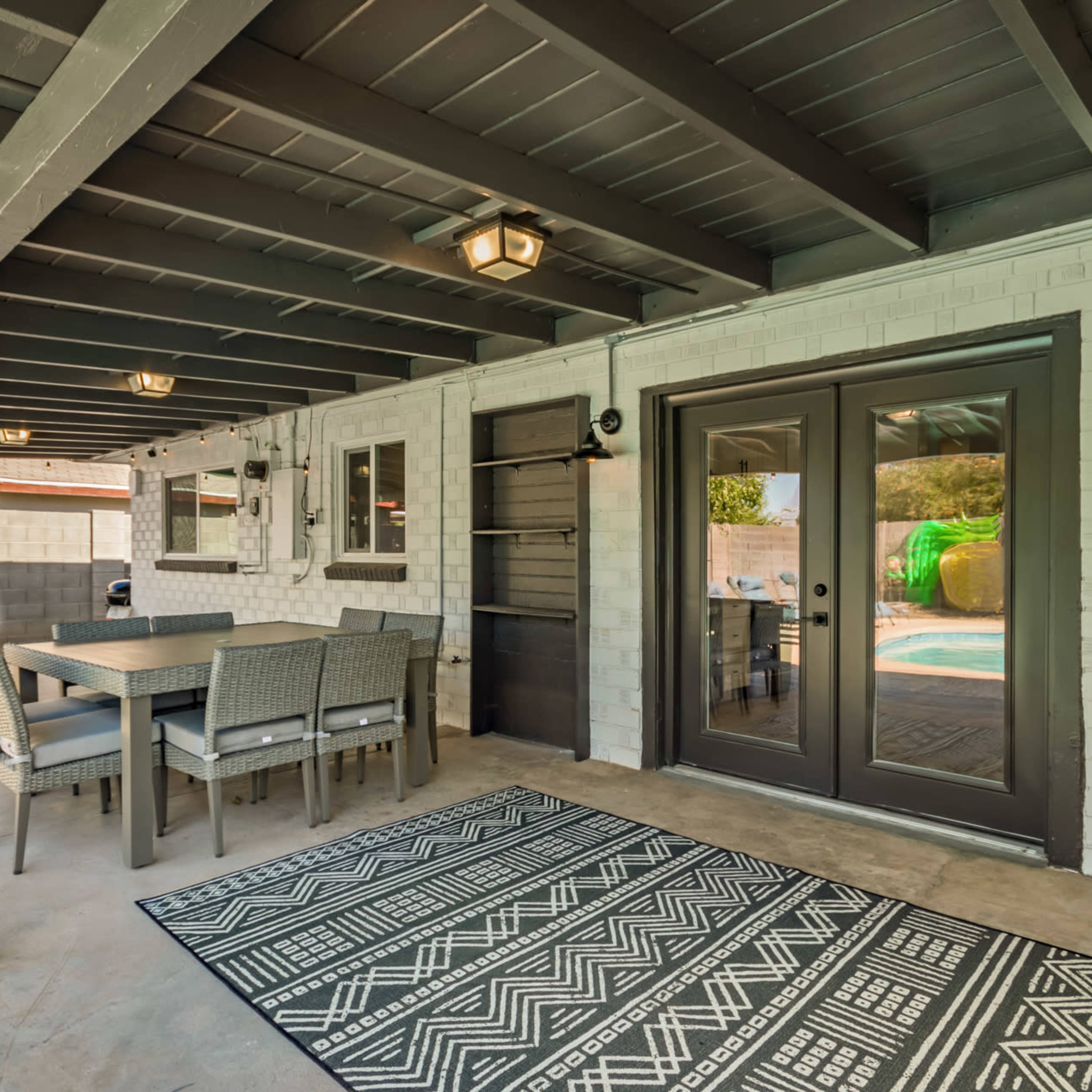 A covered patio area featuring a table and chairs, a patterned rug, and sliding glass doors that open to a pool area.