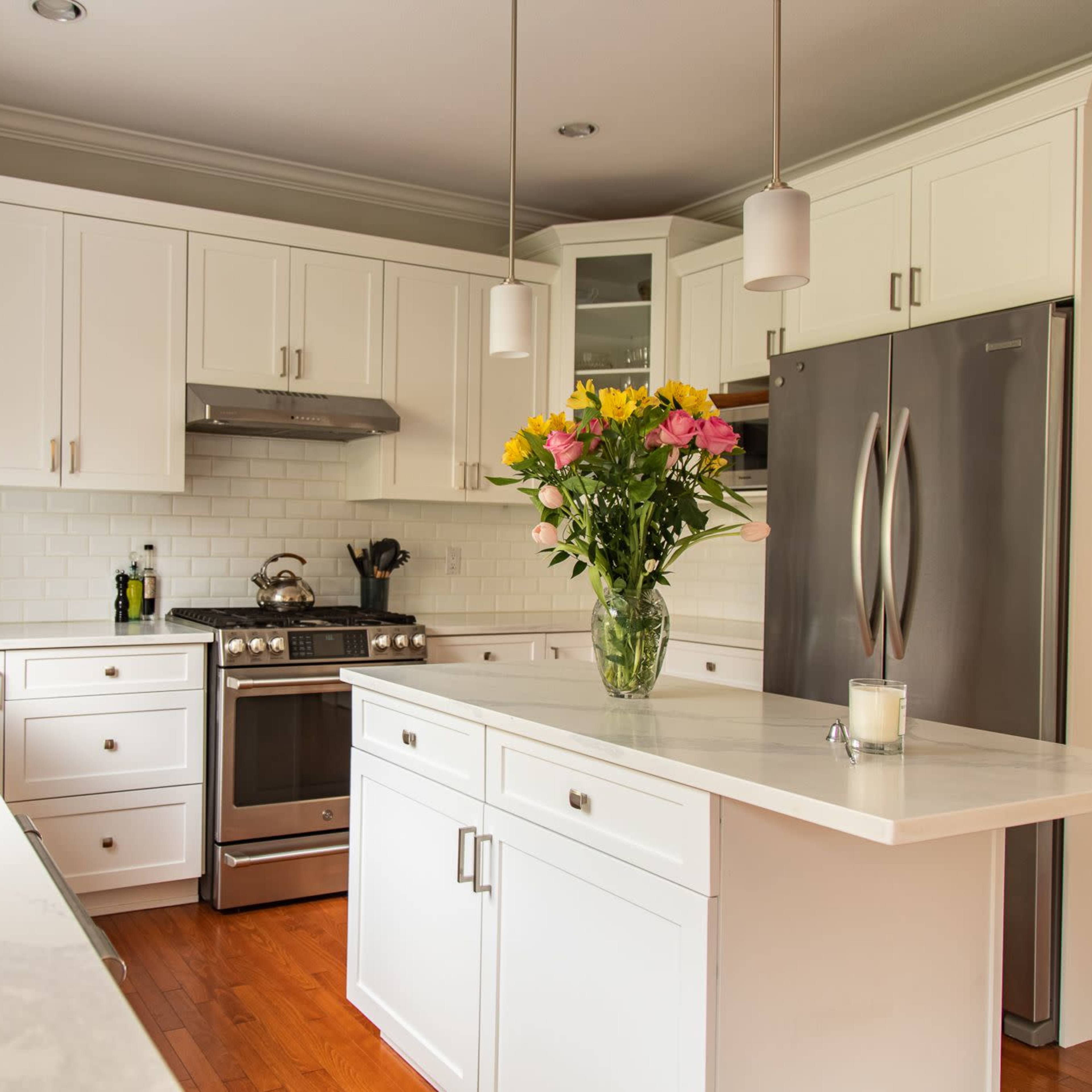 A modern kitchen features white cabinets, stainless steel appliances, and a central island with a vase of flowers.