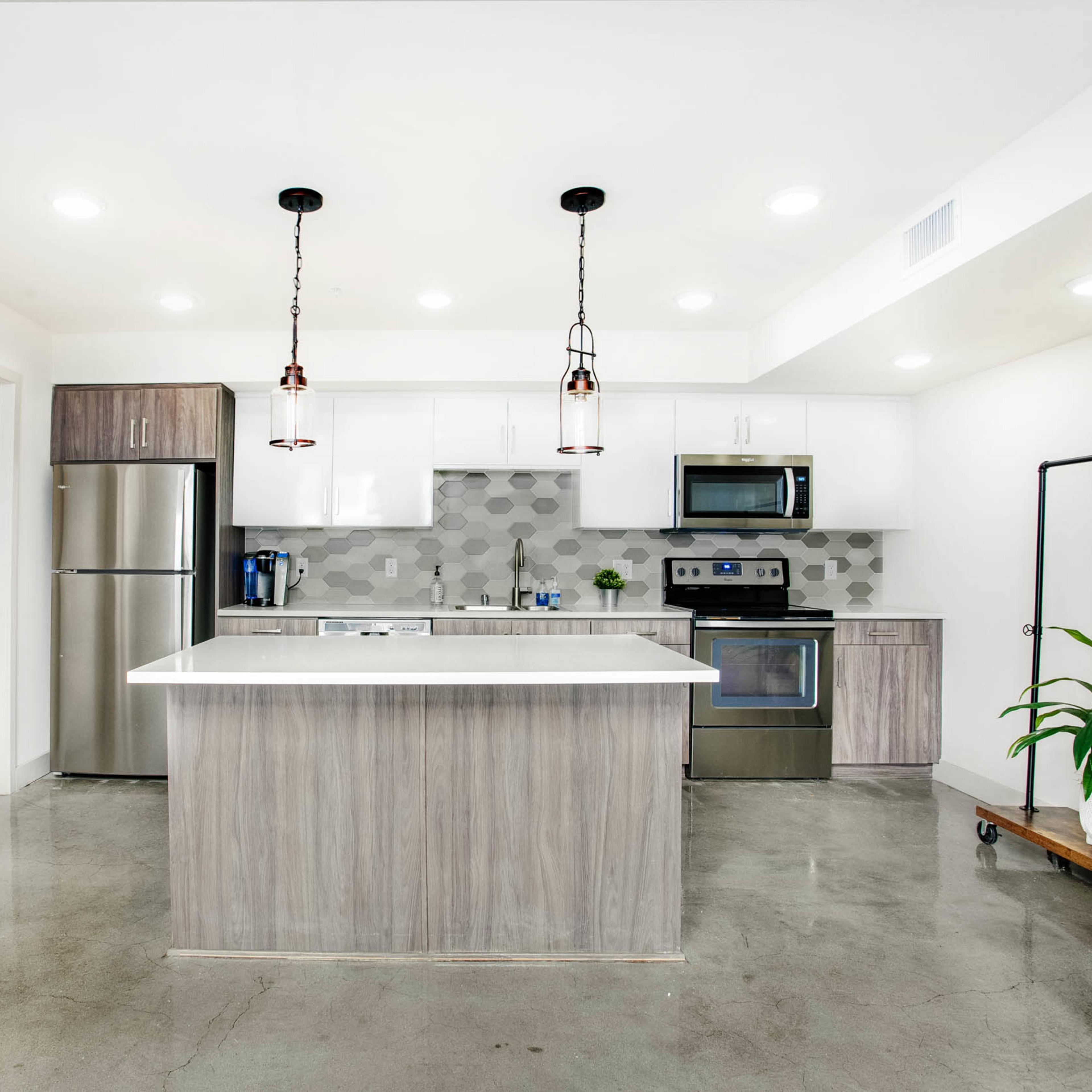 A modern kitchen features a central island, stainless steel appliances, and light-colored cabinetry with a geometric tile backsplash.