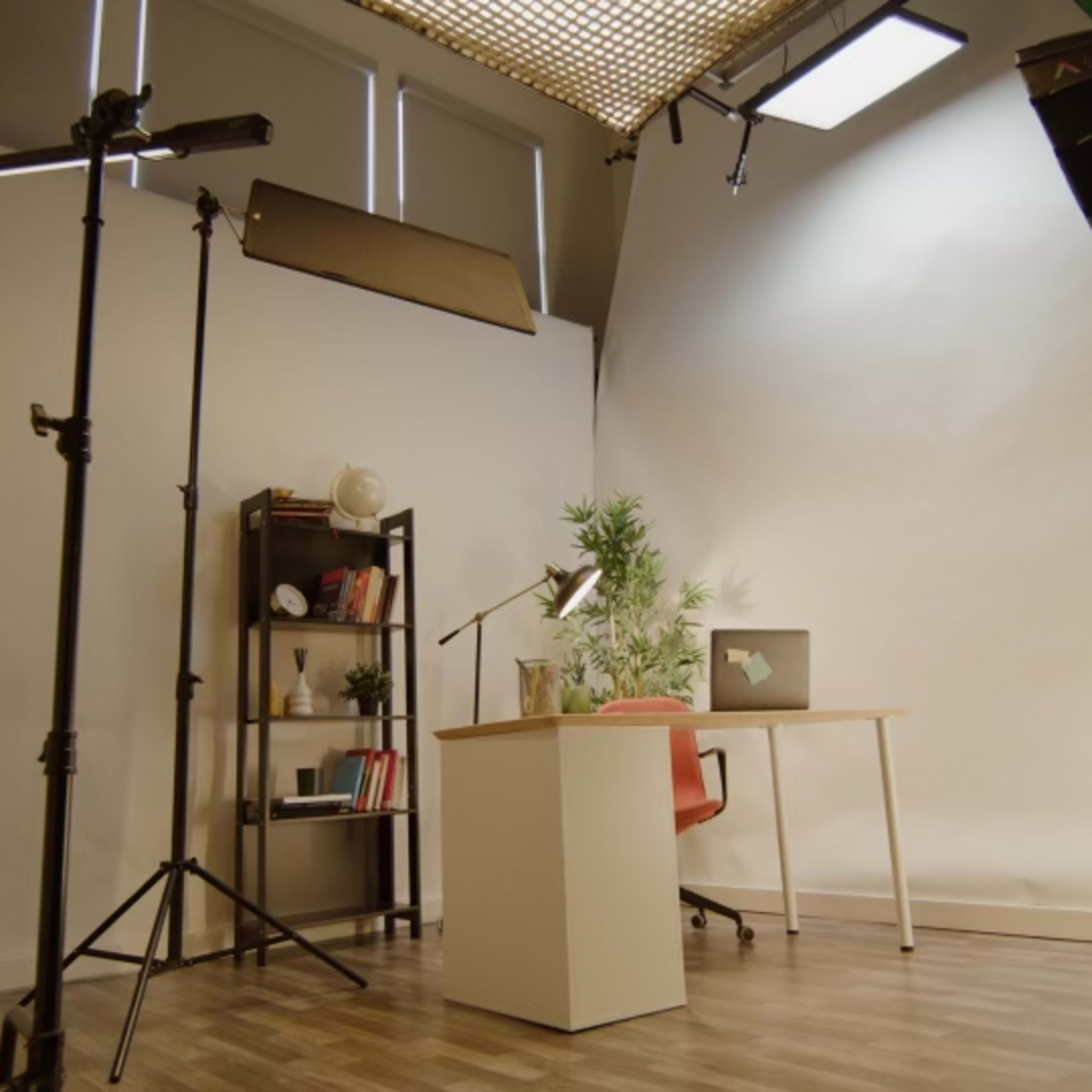 A photography studio setup with a desk, chair, lighting equipment, and a backdrop.