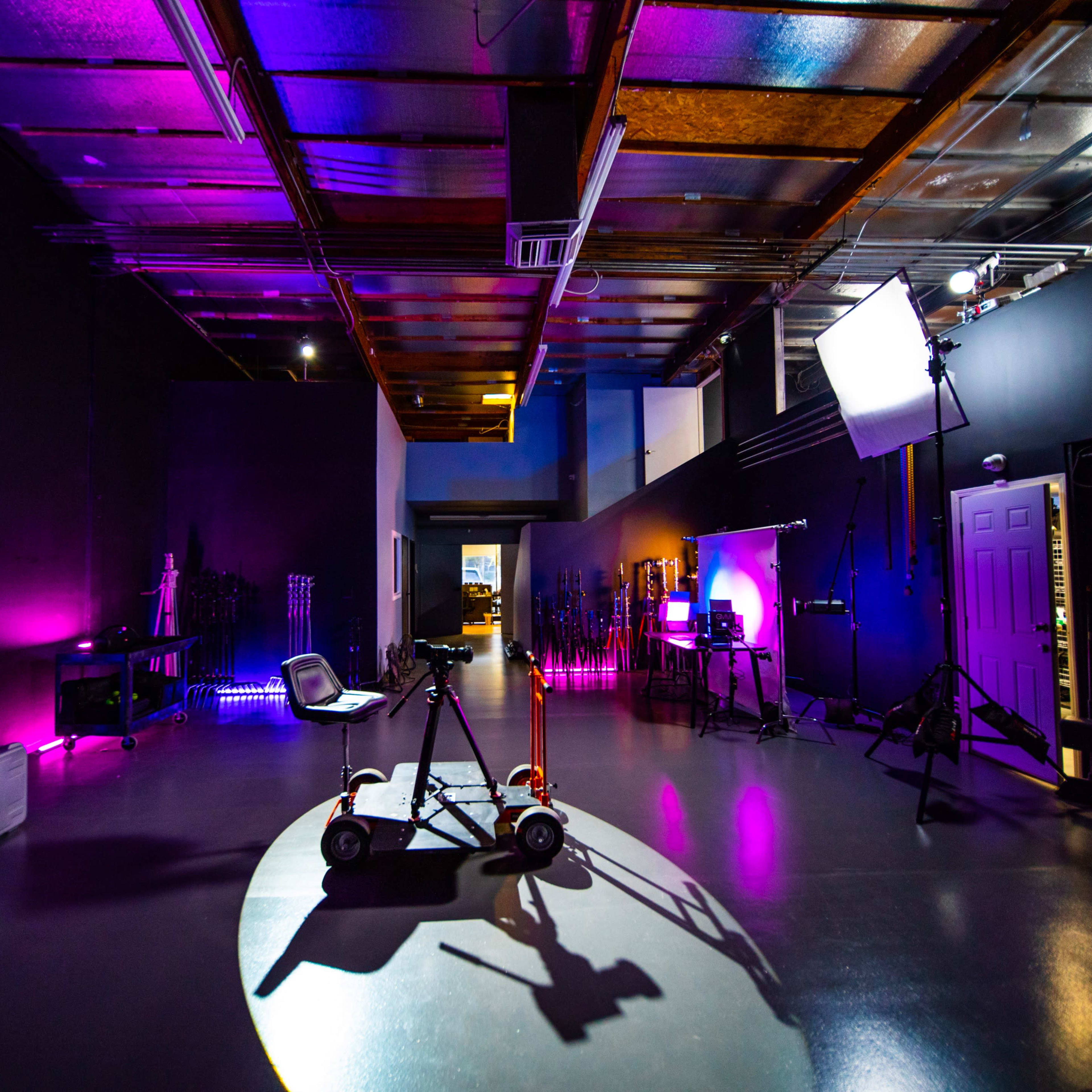 A spacious studio with various lighting equipment and a rolling camera cart positioned in a circular pool of light.