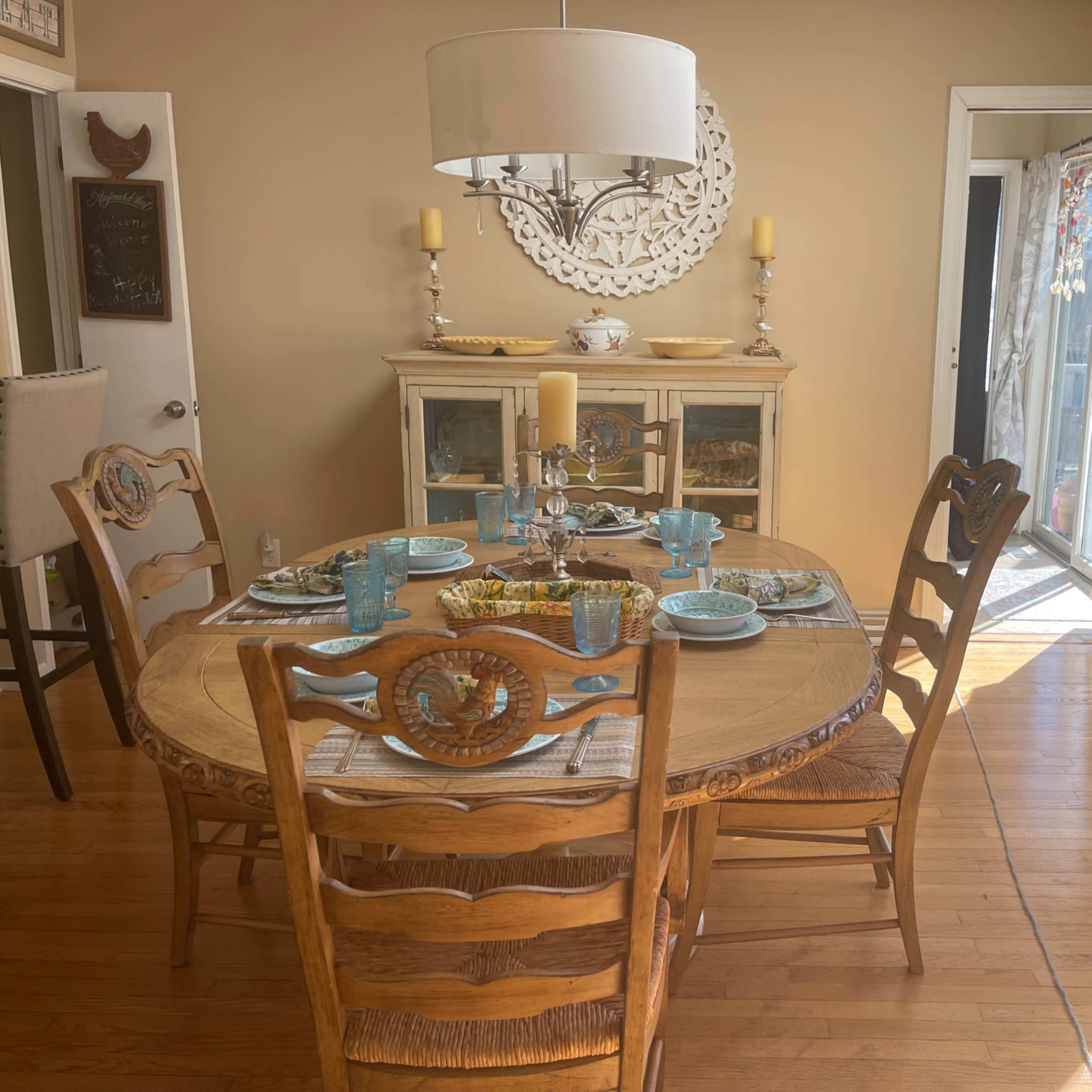 A round dining table is set with plates and glasses in a bright room featuring a cabinet and sliding glass doors.