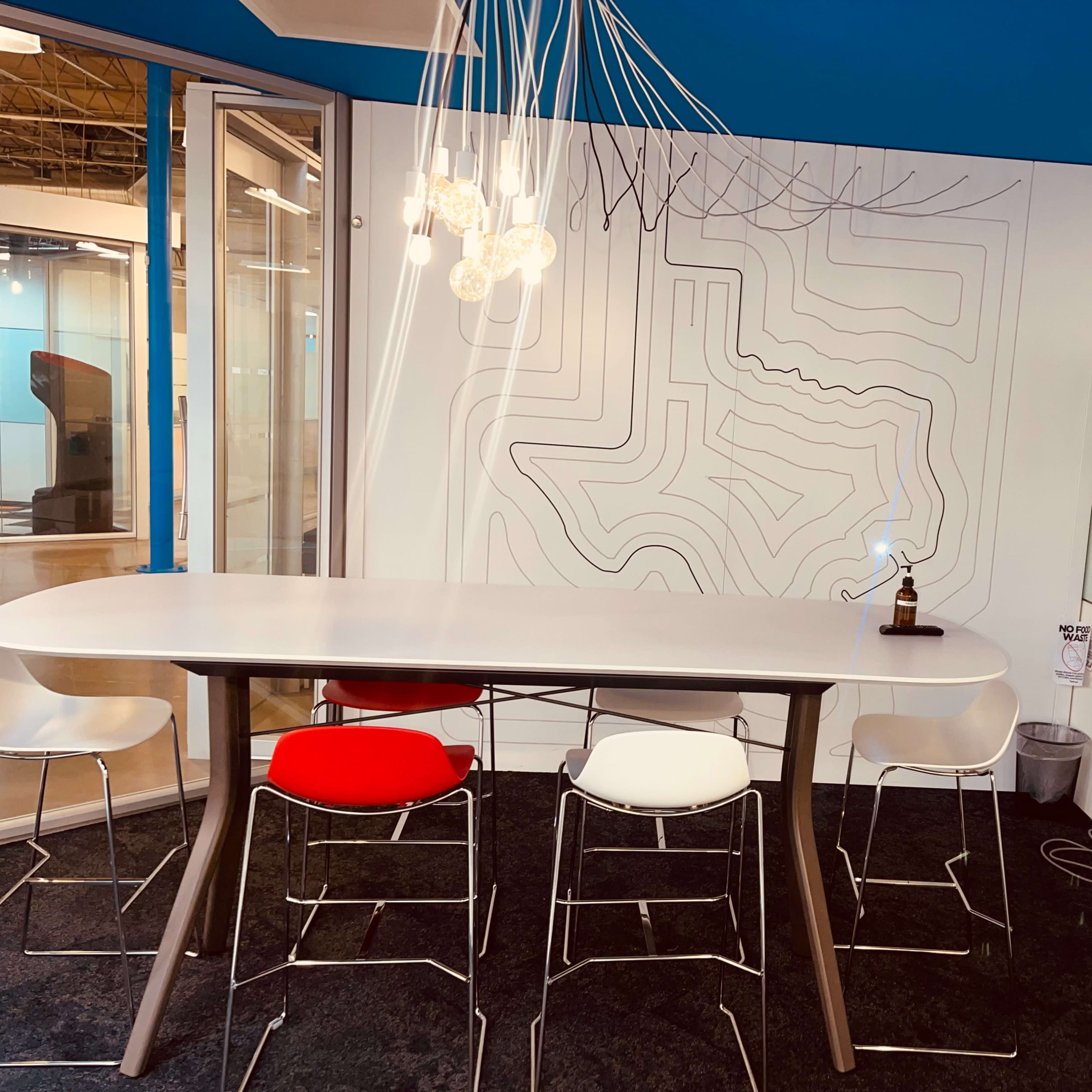 A modern meeting room features a sleek table with white, red, and black chairs, a television on the wall, and a decorative light fixture above.